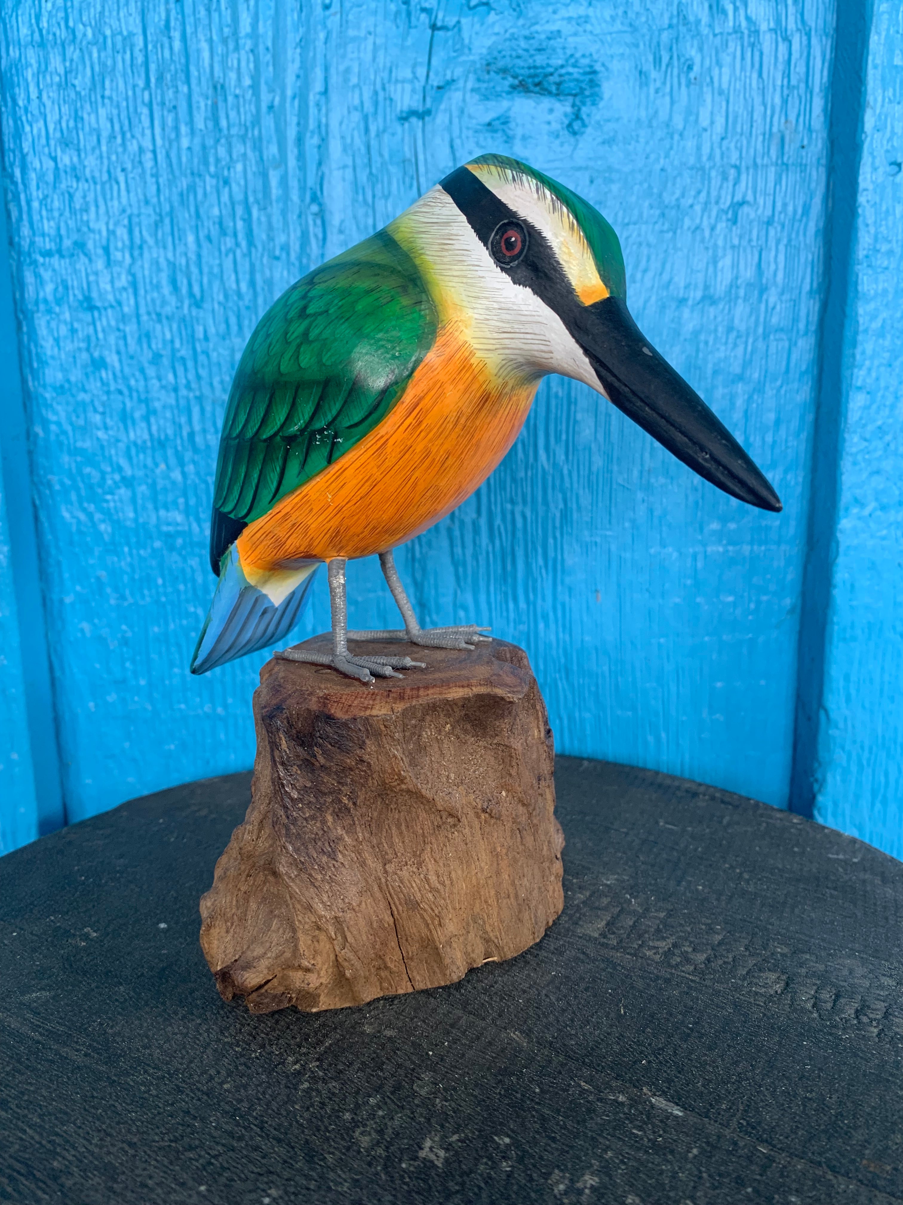colorful wooden kingfisher sculpture perched on a log against a blue background