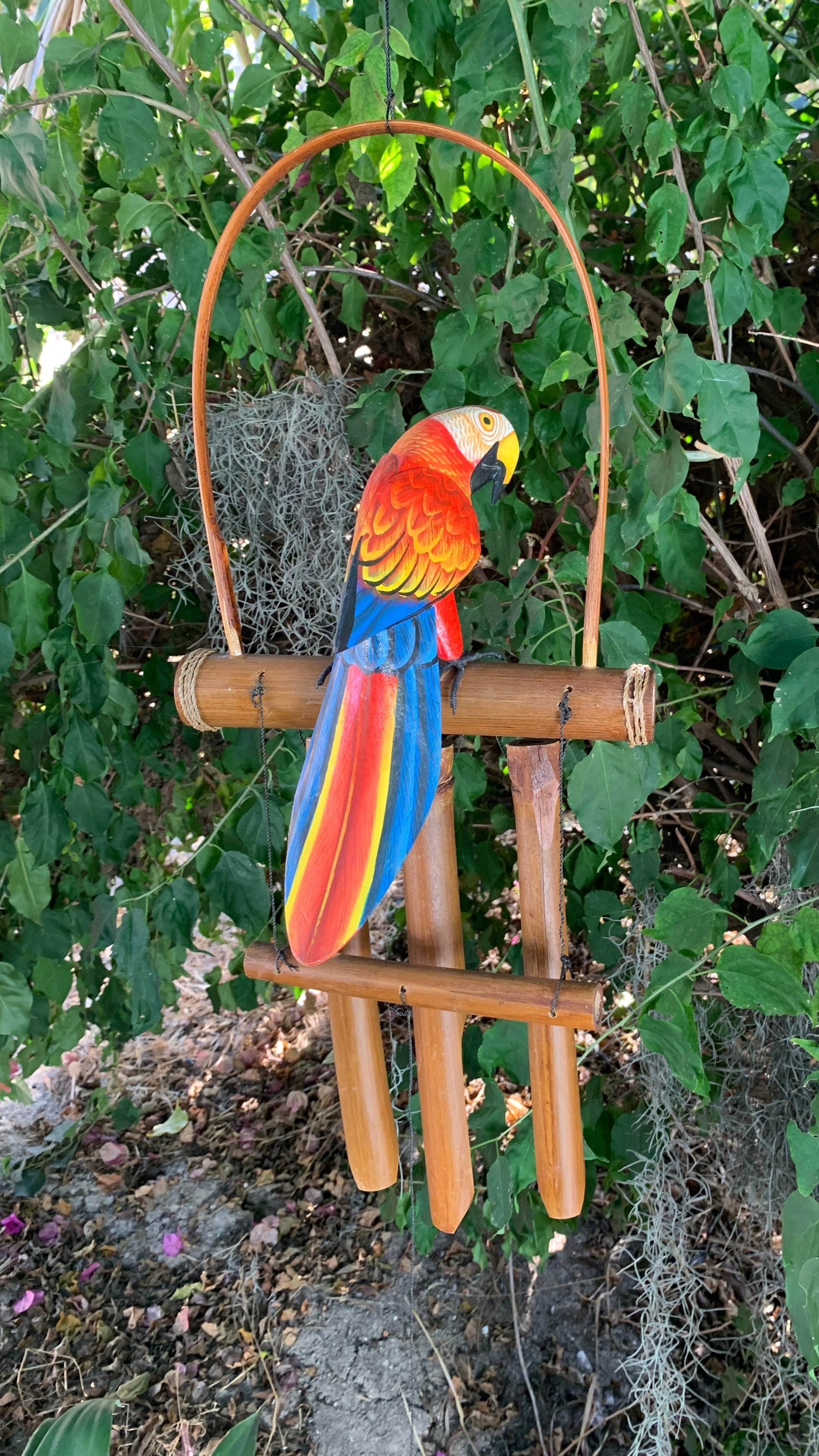 Colorful macaw parrot statue perched on wooden wind chime in a garden