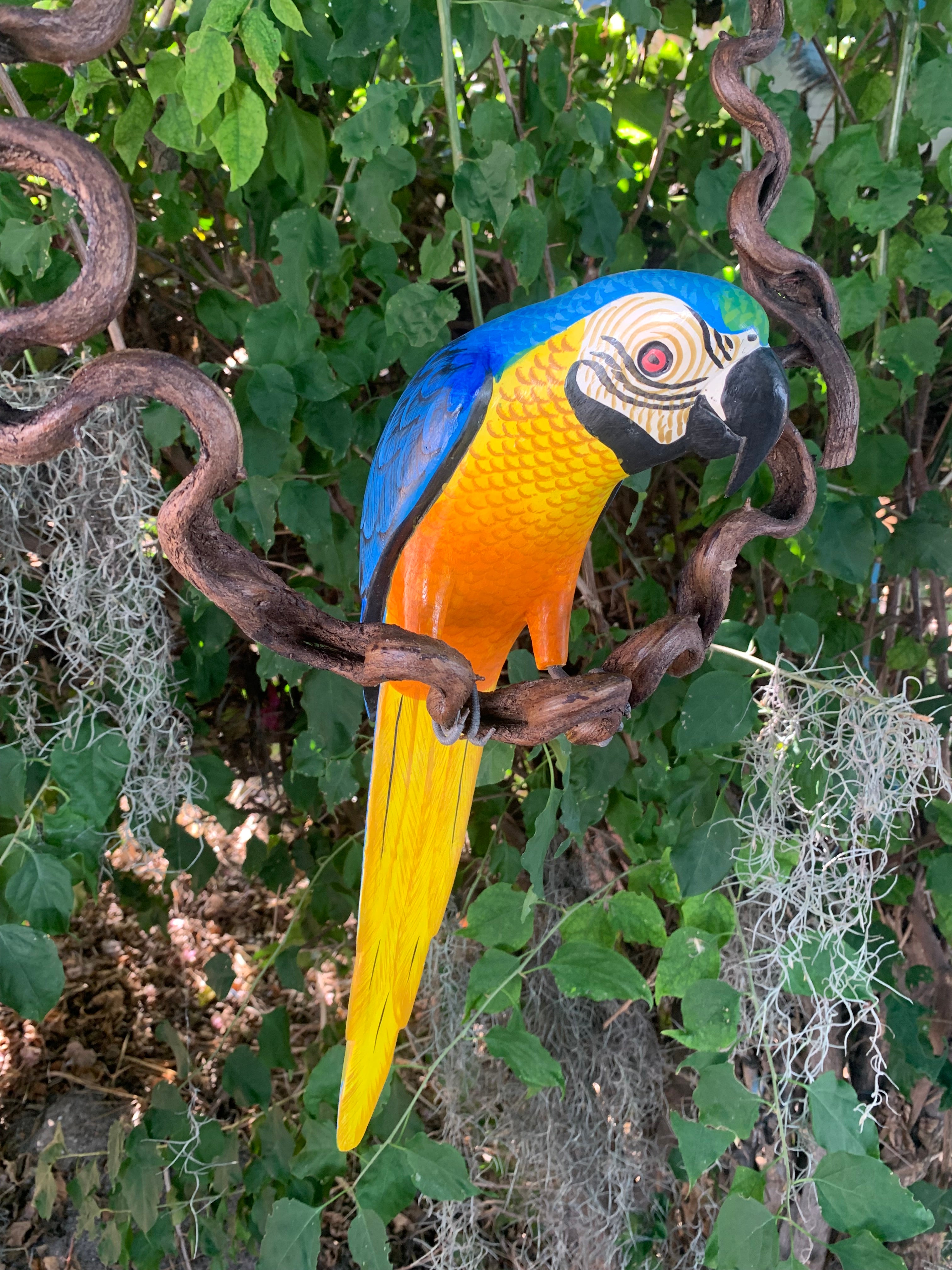Colorful macaw sculpture perched on a twisted branch in a garden