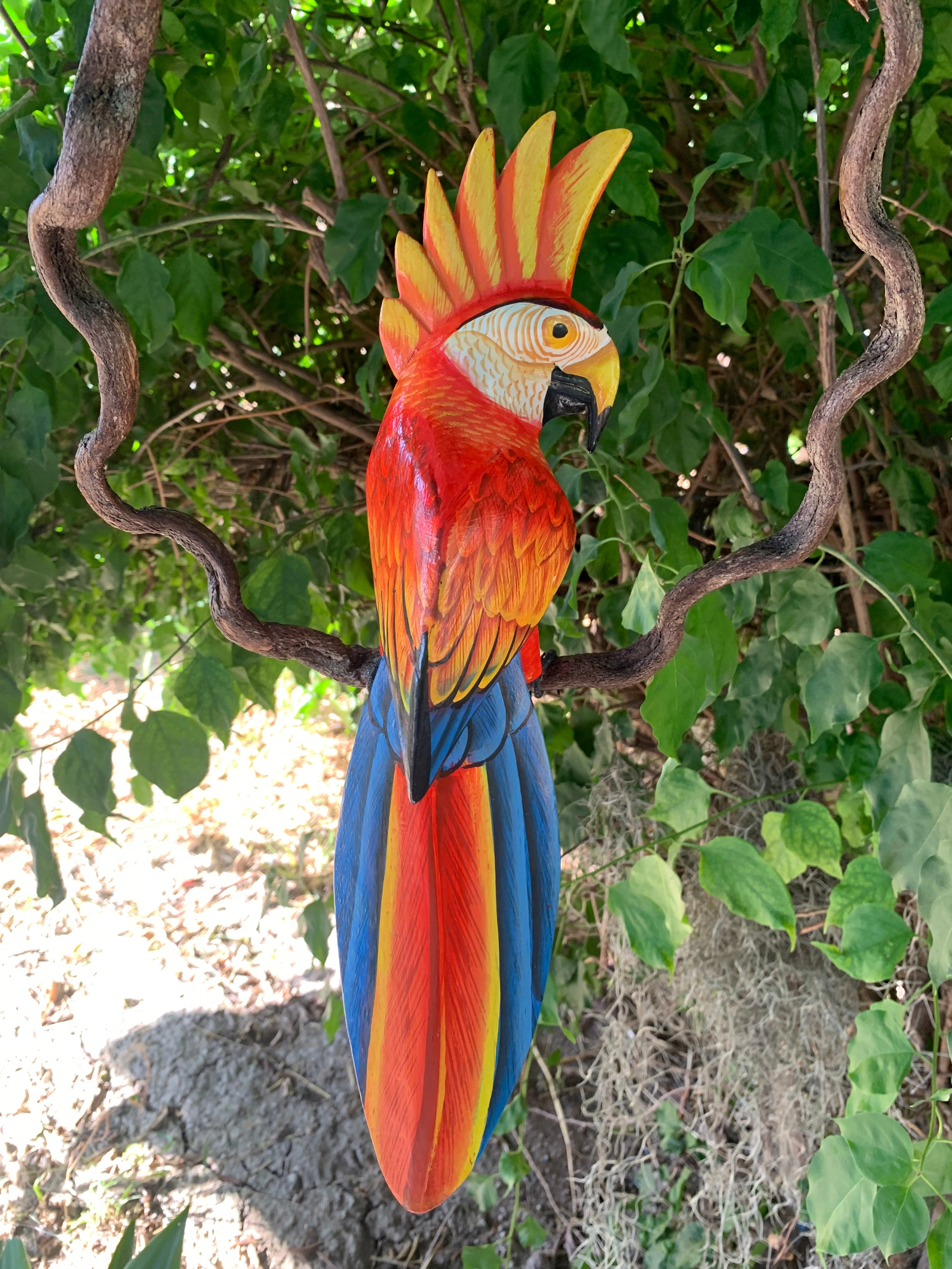 Colorful macaw sculpture perched on a twisting branch among green leaves.