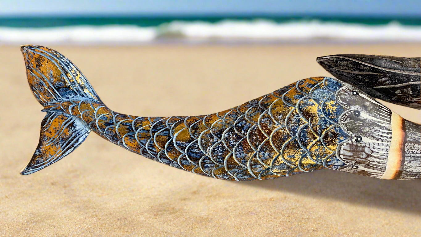 Colorful mermaid tail sculpture with detailed scales on a sandy beach with the ocean in the background.