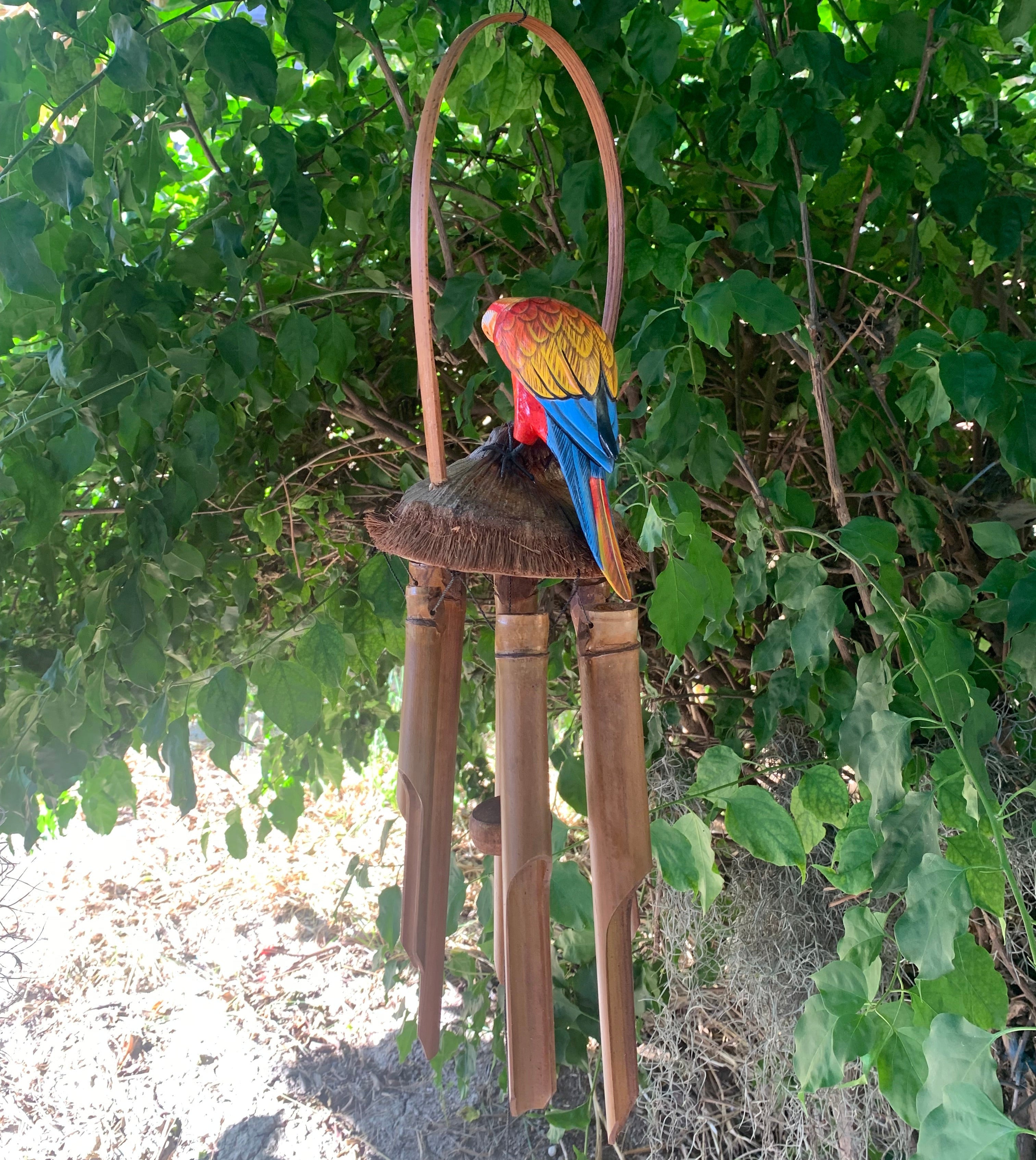 Colorful parrot statue perched on a bamboo wind chime in a leafy garden.