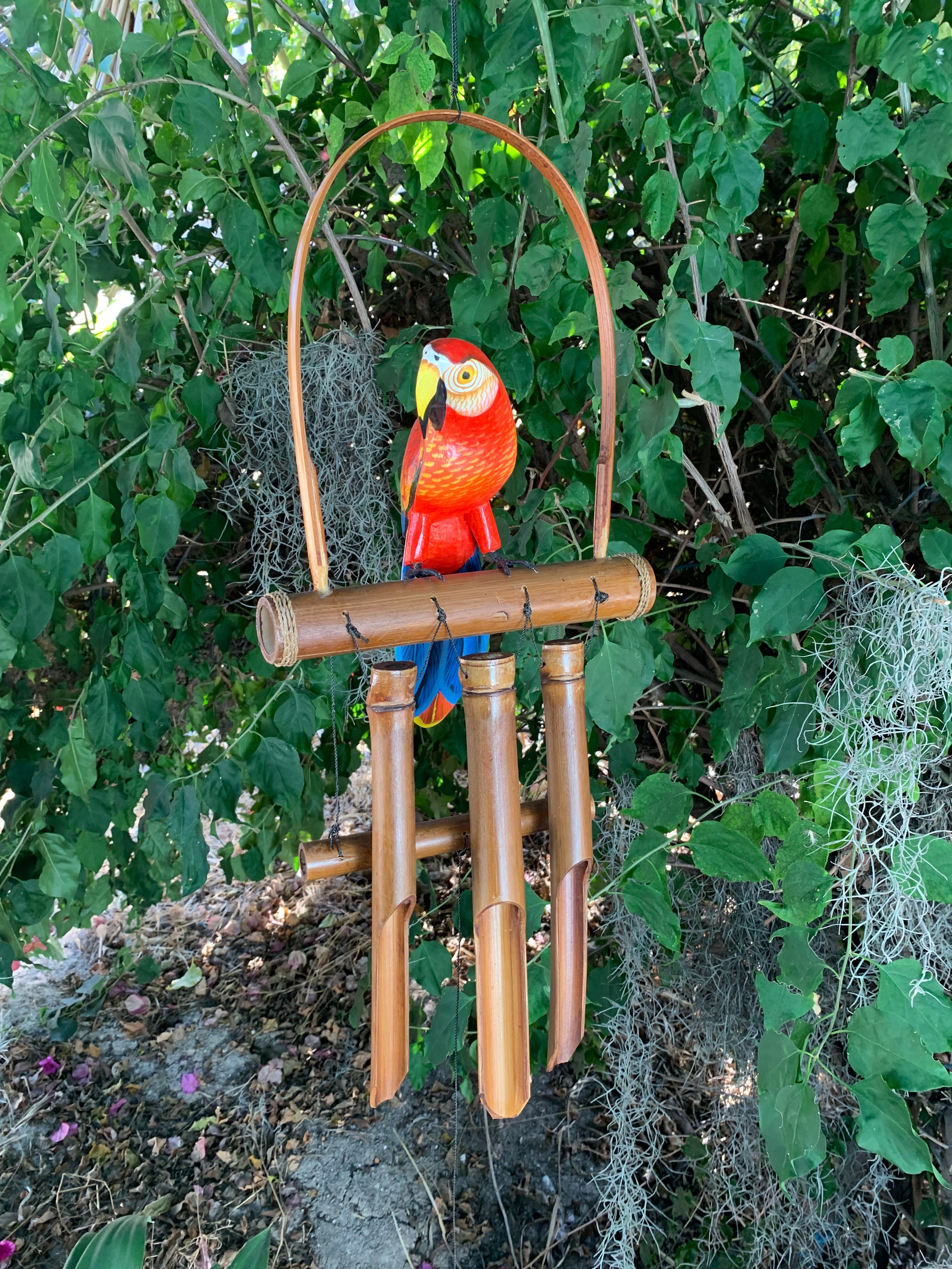 Colorful parrot sculpture perched on bamboo wind chimes in a garden