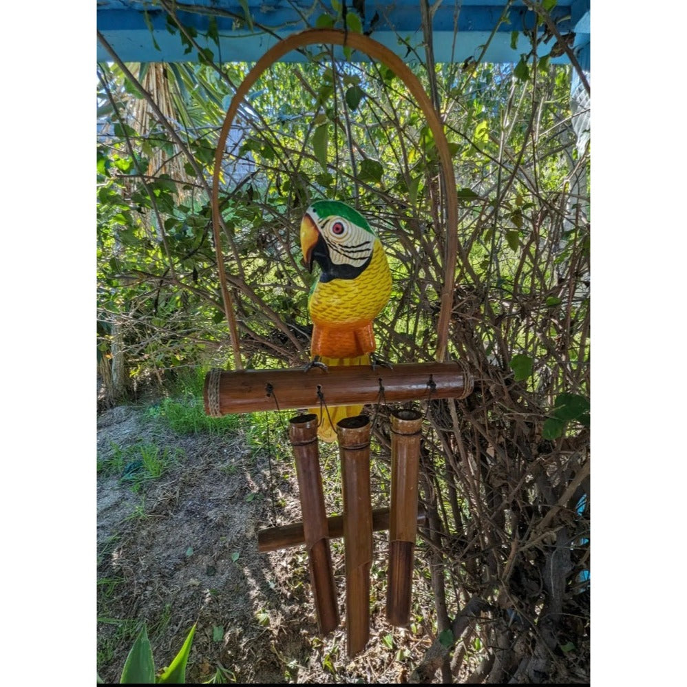 Colorful parrot sculpture perched on a bamboo wind-chime frame in a garden.