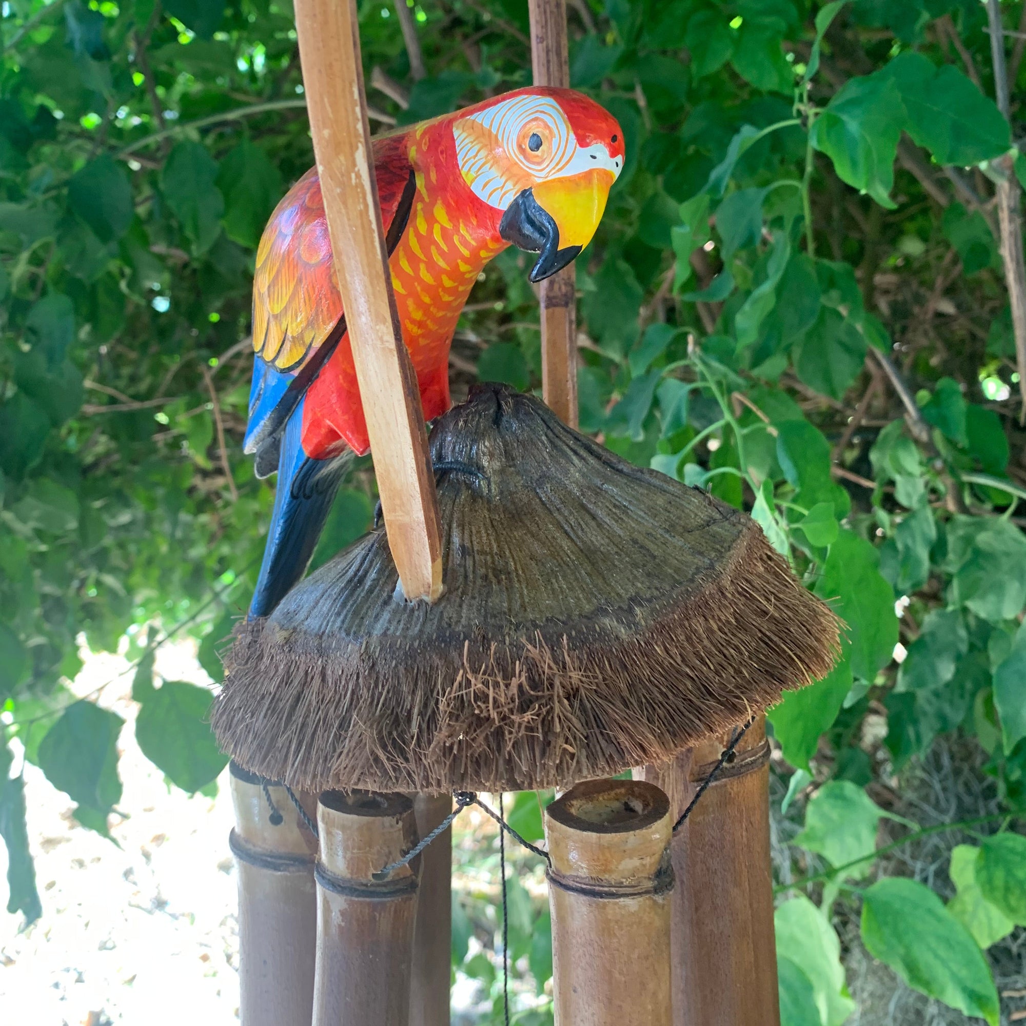 colorful parrot garden ornament perched on a thatched roof with bamboo posts