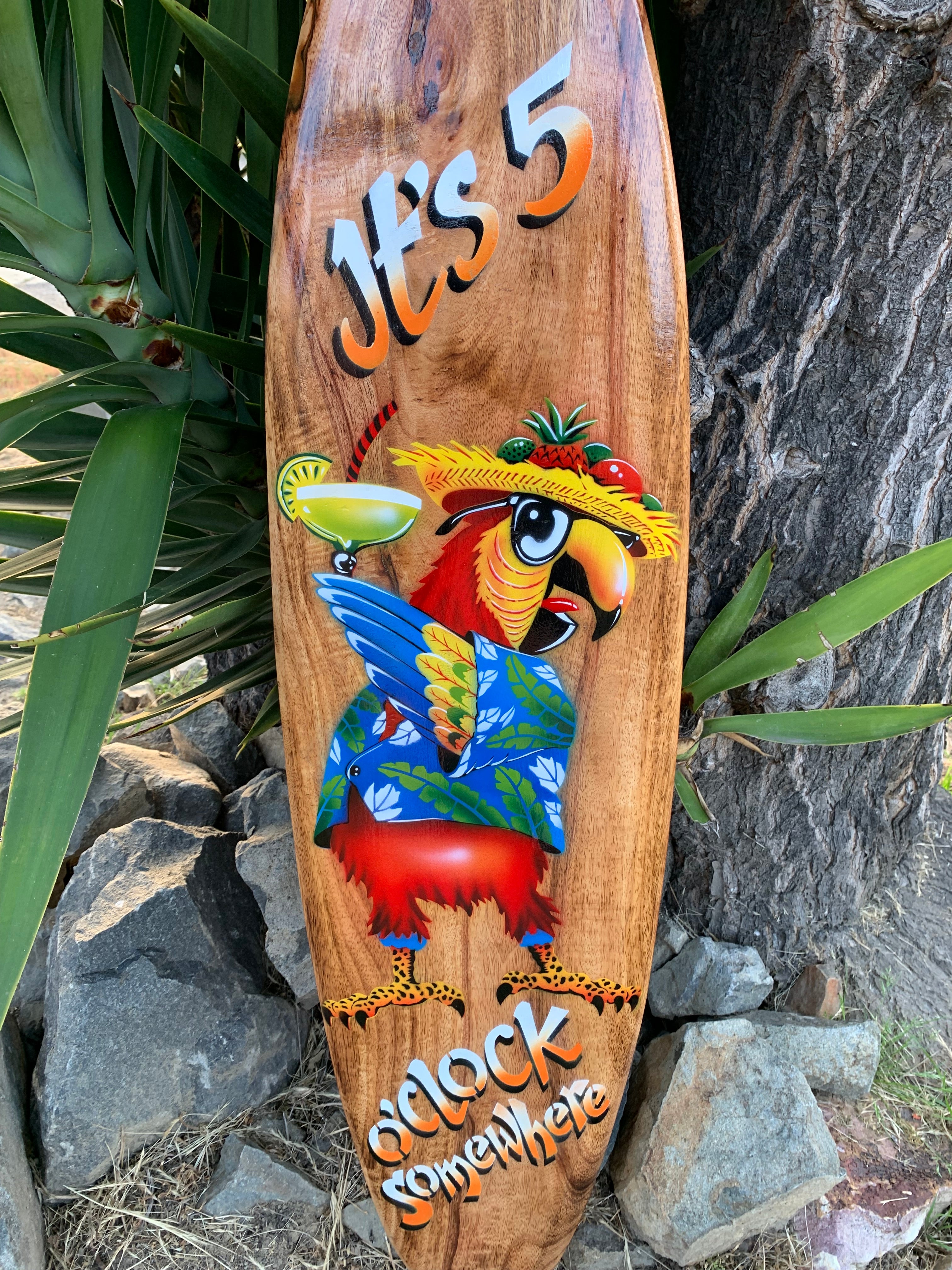 Colorful parrot wearing a straw hat and Hawaiian shirt on a wooden surfboard with a tropical cocktail