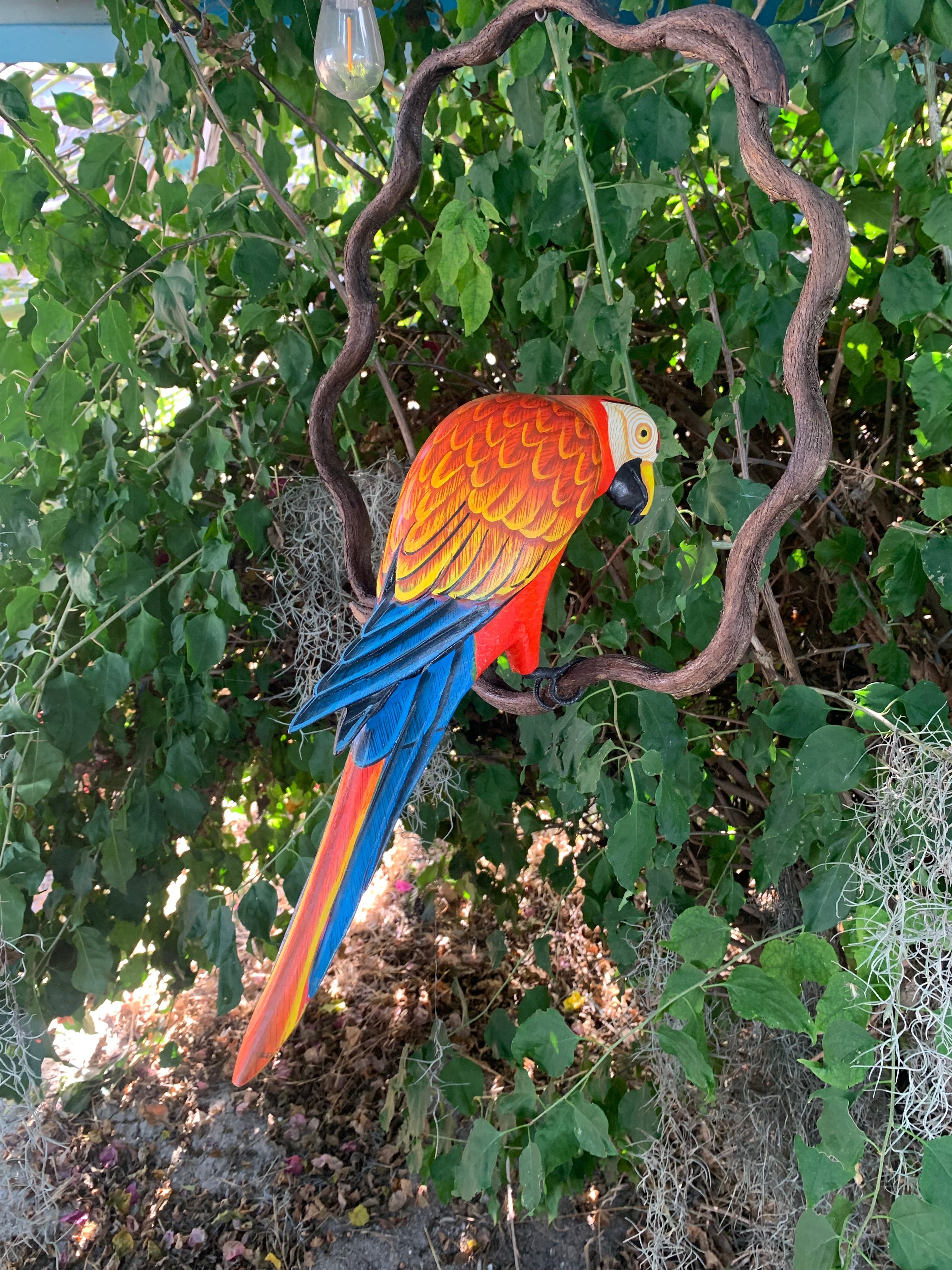 Colorful parrot sculpture perched on a twisting branch among green leaves.