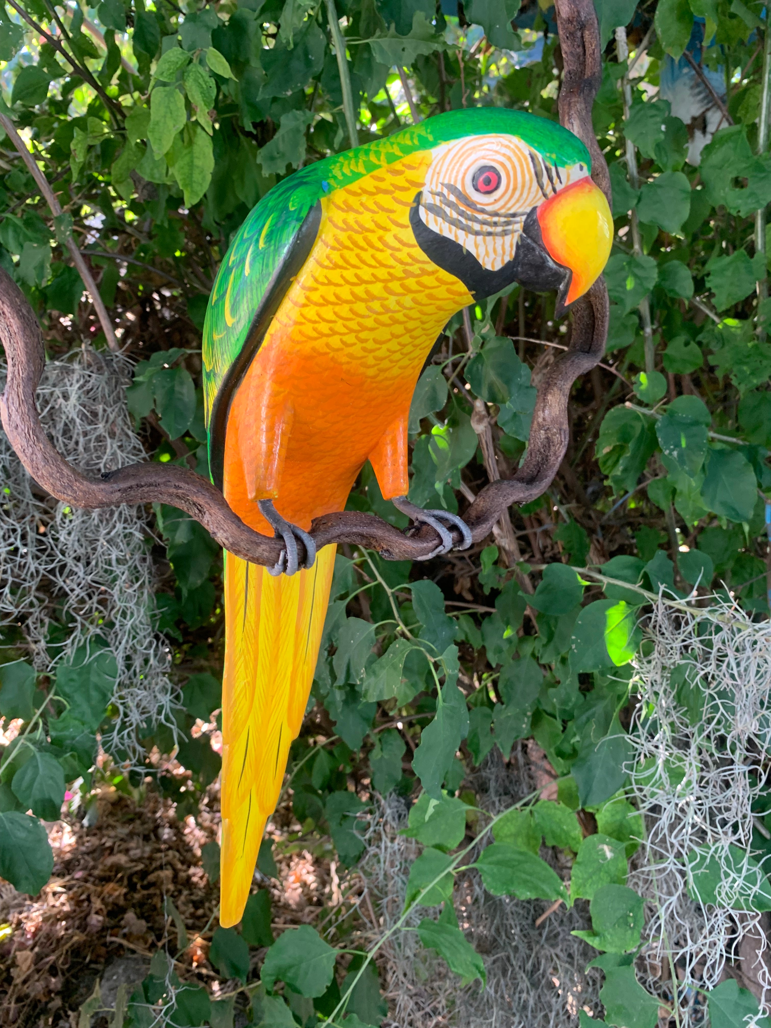 colorful parrot sculpture perched on a branch among green foliage