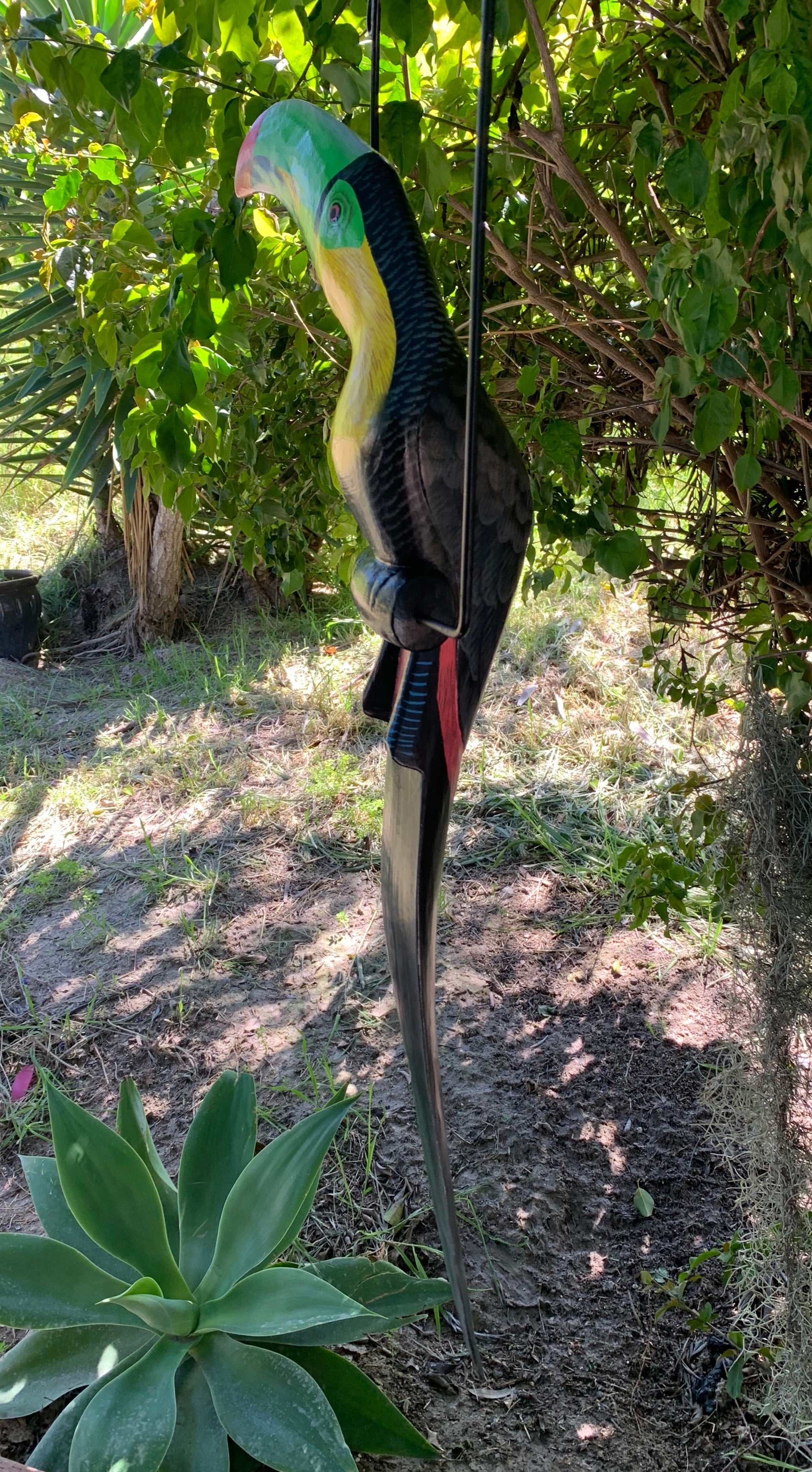 Colorful parrot sculpture perched in a garden with green leaves
