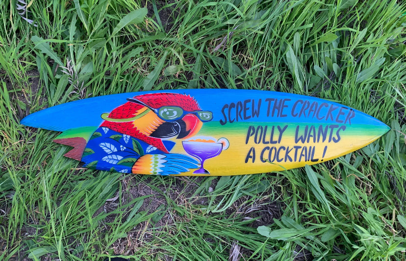 Colorful parrot-themed surfboard on grass with a cocktail illustration and bold text