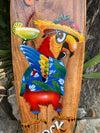 Colorful cartoon parrot in a straw hat and blue Hawaiian shirt, holding a cocktail on a wooden sign.