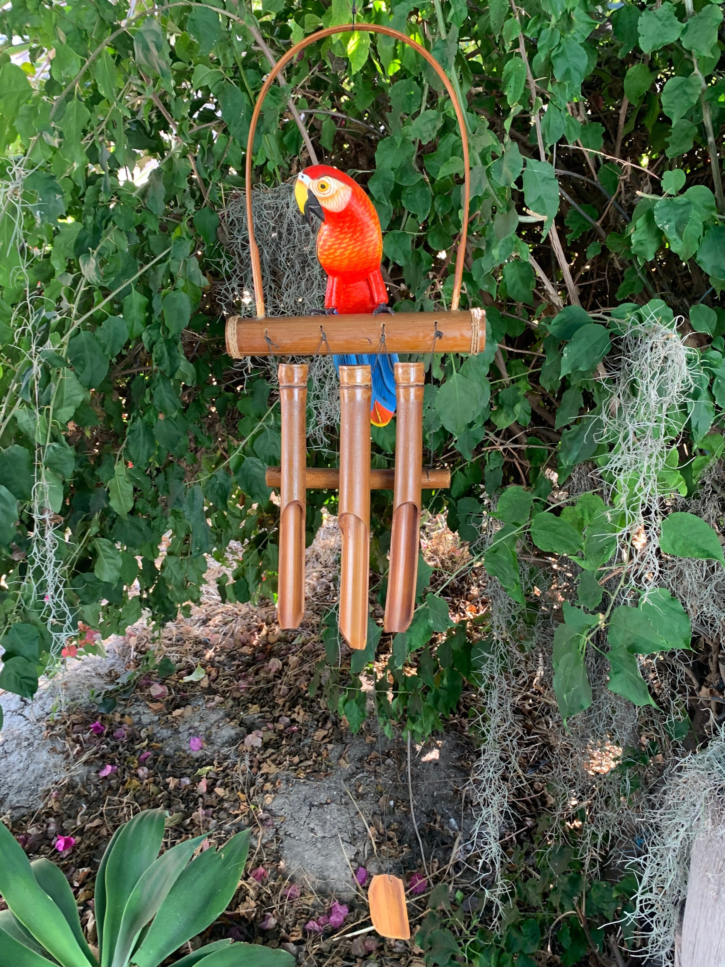 colorful parrot wind chime with bamboo tubes hanging in a leafy garden