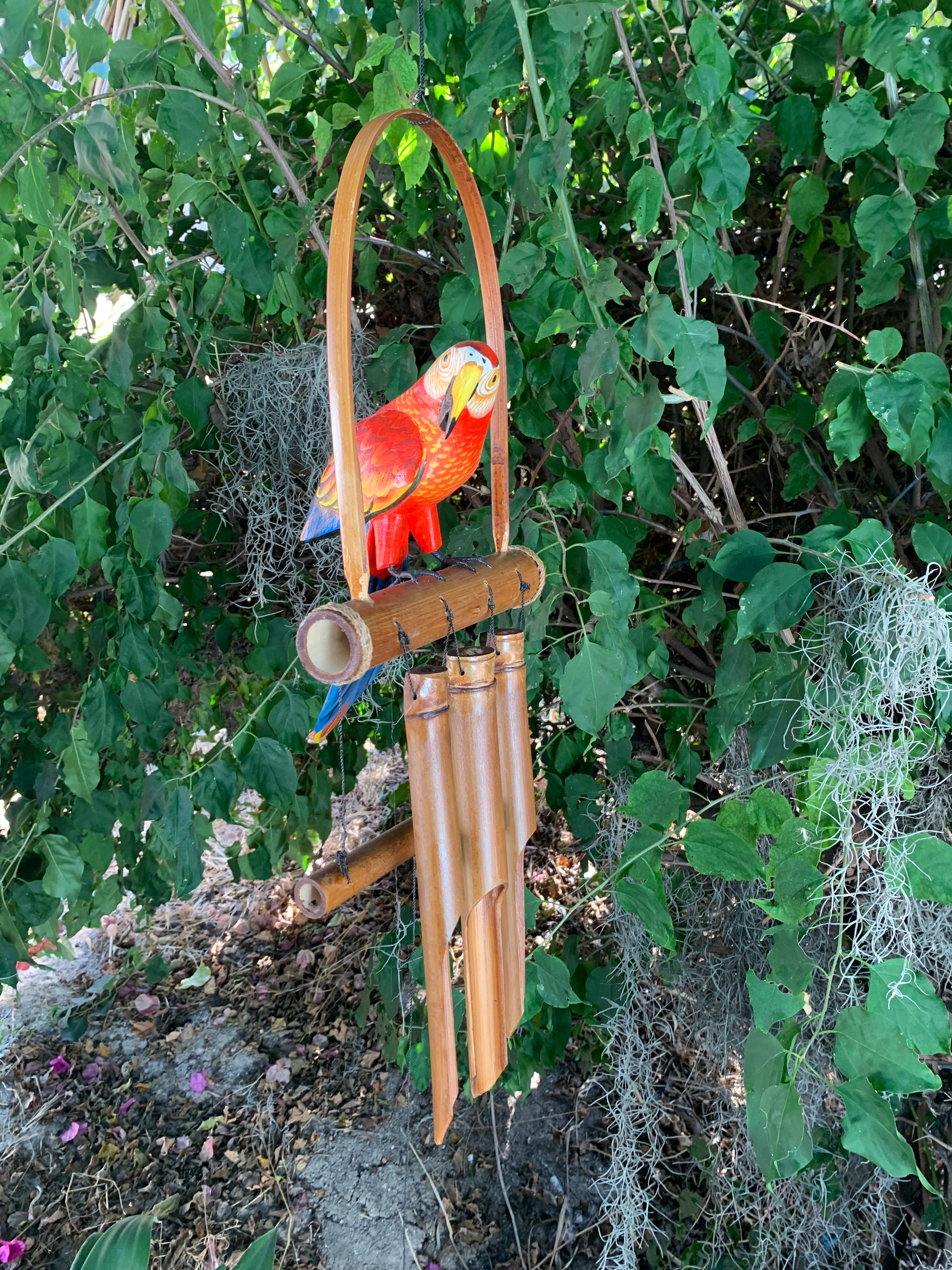 Colorful parrot wind chime perched on a bamboo arch in a leafy garden