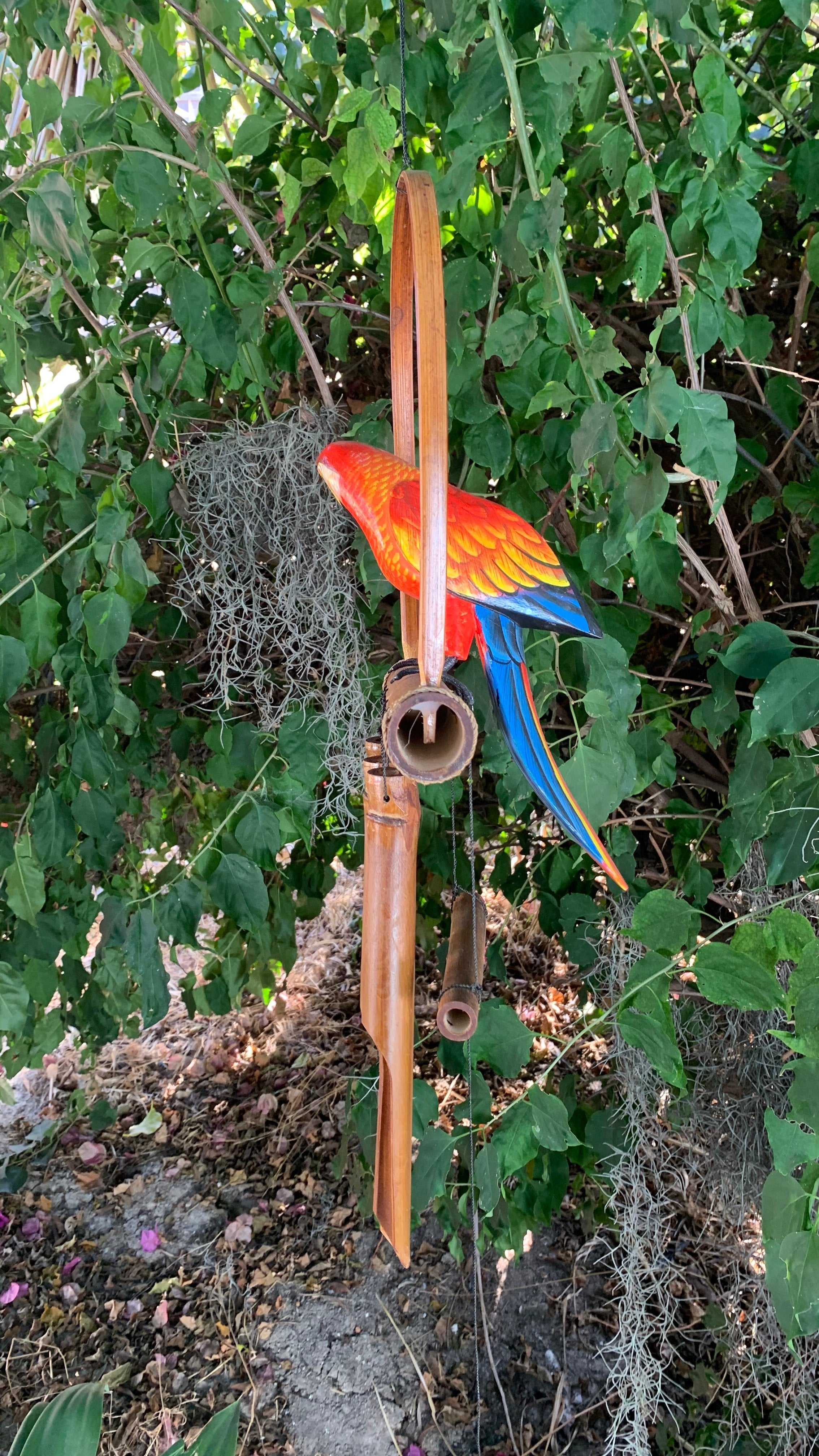 Colorful parrot wind chime hanging in a garden with green foliage