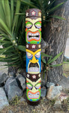 Colorful carved tiki totem pole with flower motifs beside rocks and a tree