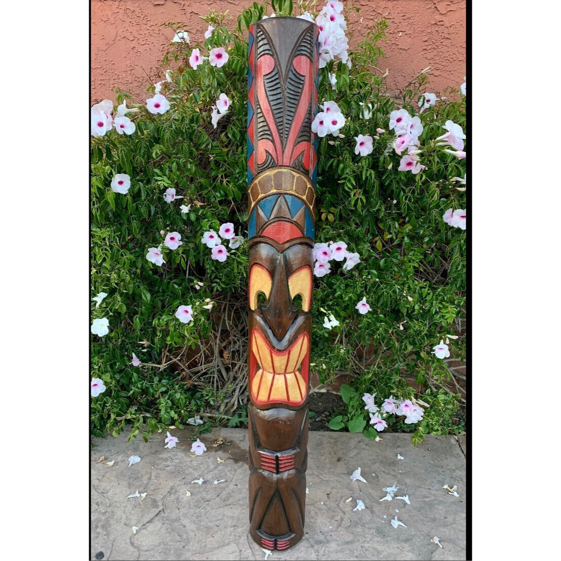 Colorful wooden tiki totem pole in front of white and pink hibiscus flowers