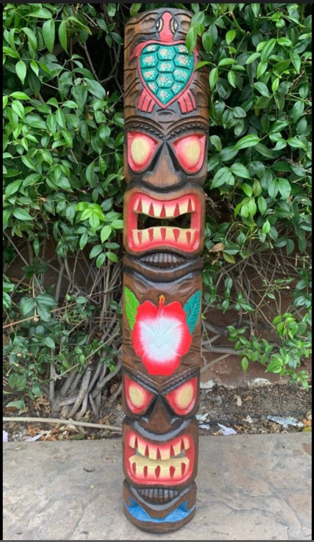 Colorful carved tiki totem pole with multiple faces and a flower motif in a leafy garden