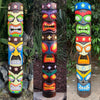 Three colorful tiki totem poles with floral decorations in a garden setting