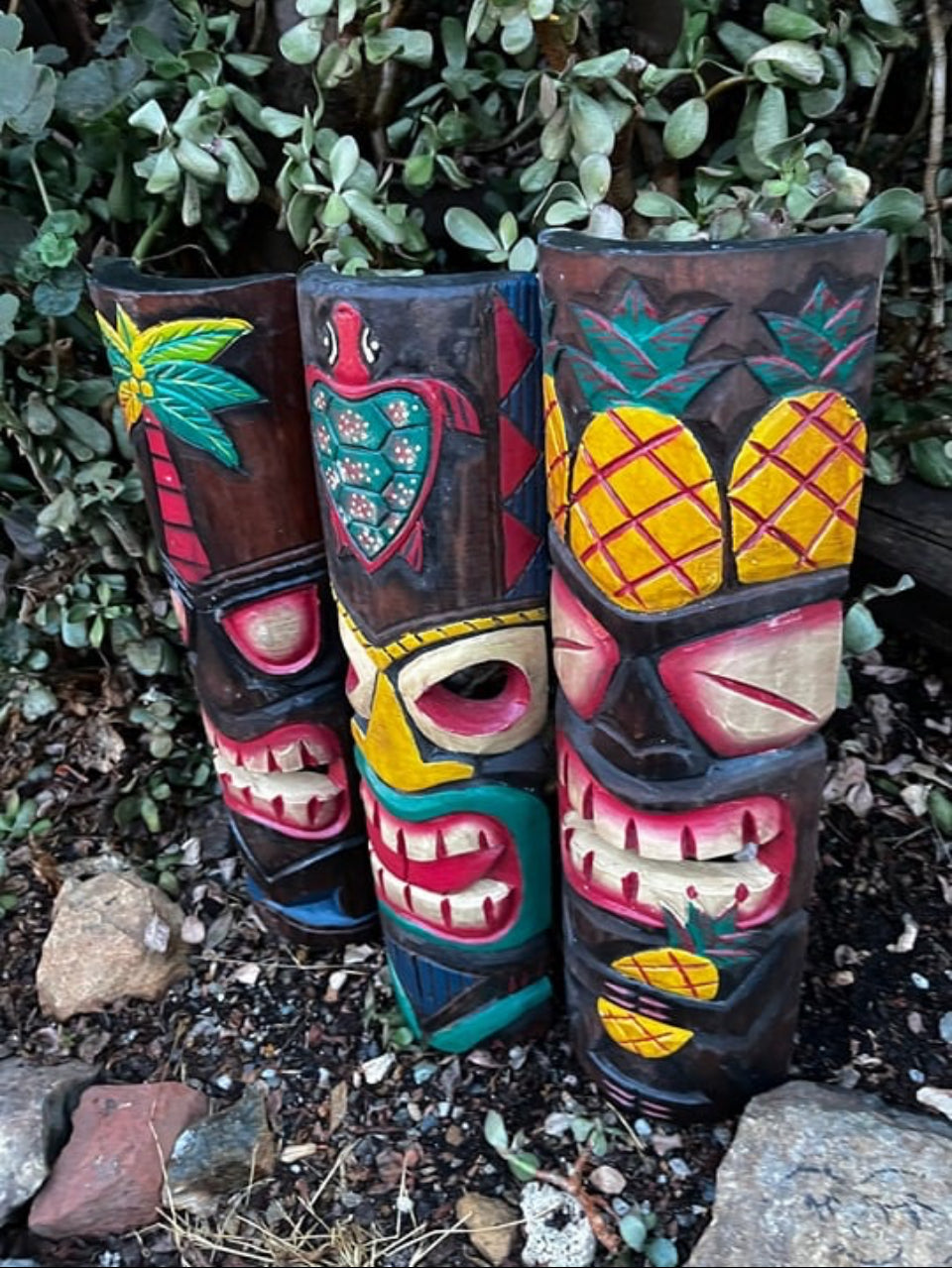 Three colorful tiki totem sculptures with pineapple patterns in a garden.