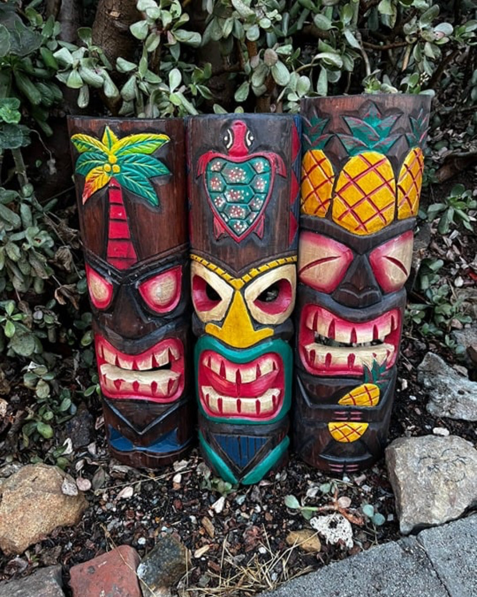 Three colorful tiki totem sculptures with tropical designs in a garden setting