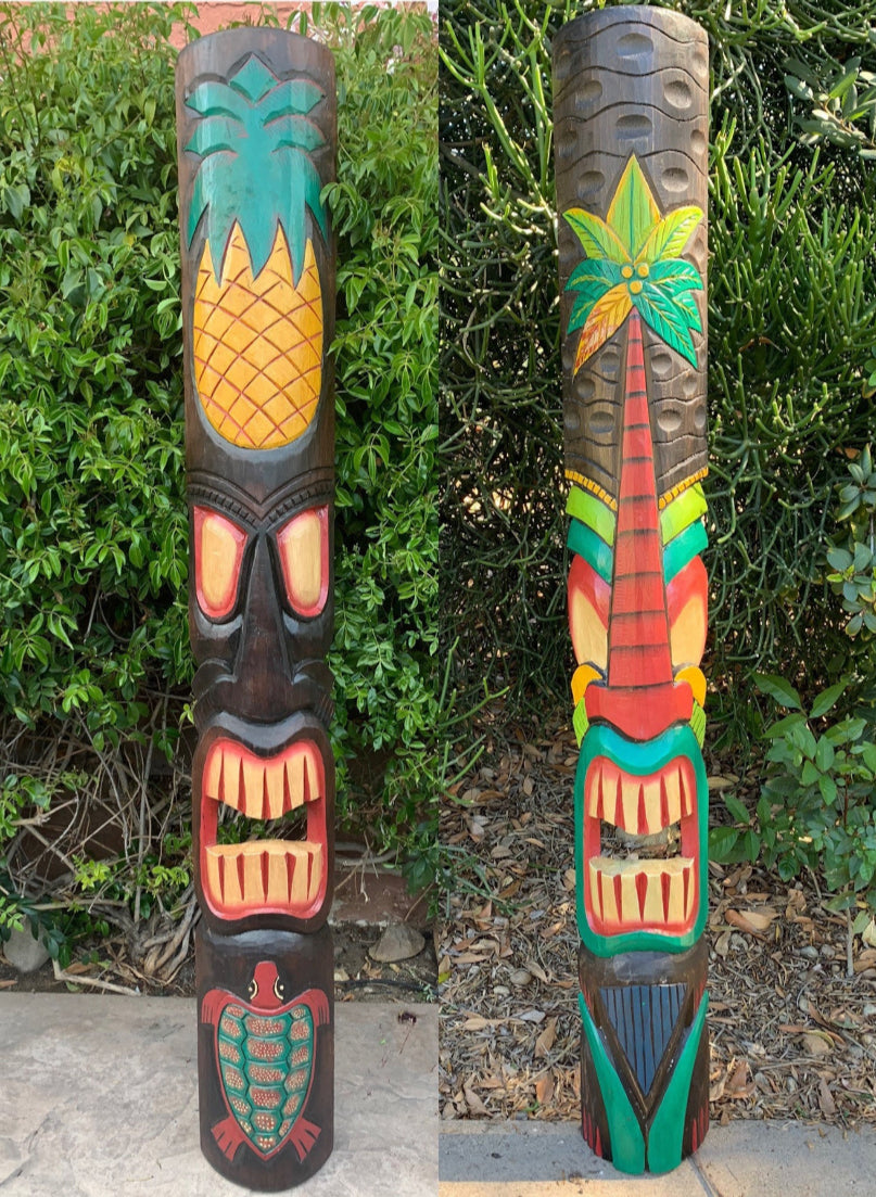 Two colorful tiki totem poles with pineapple and palm tree designs in a garden