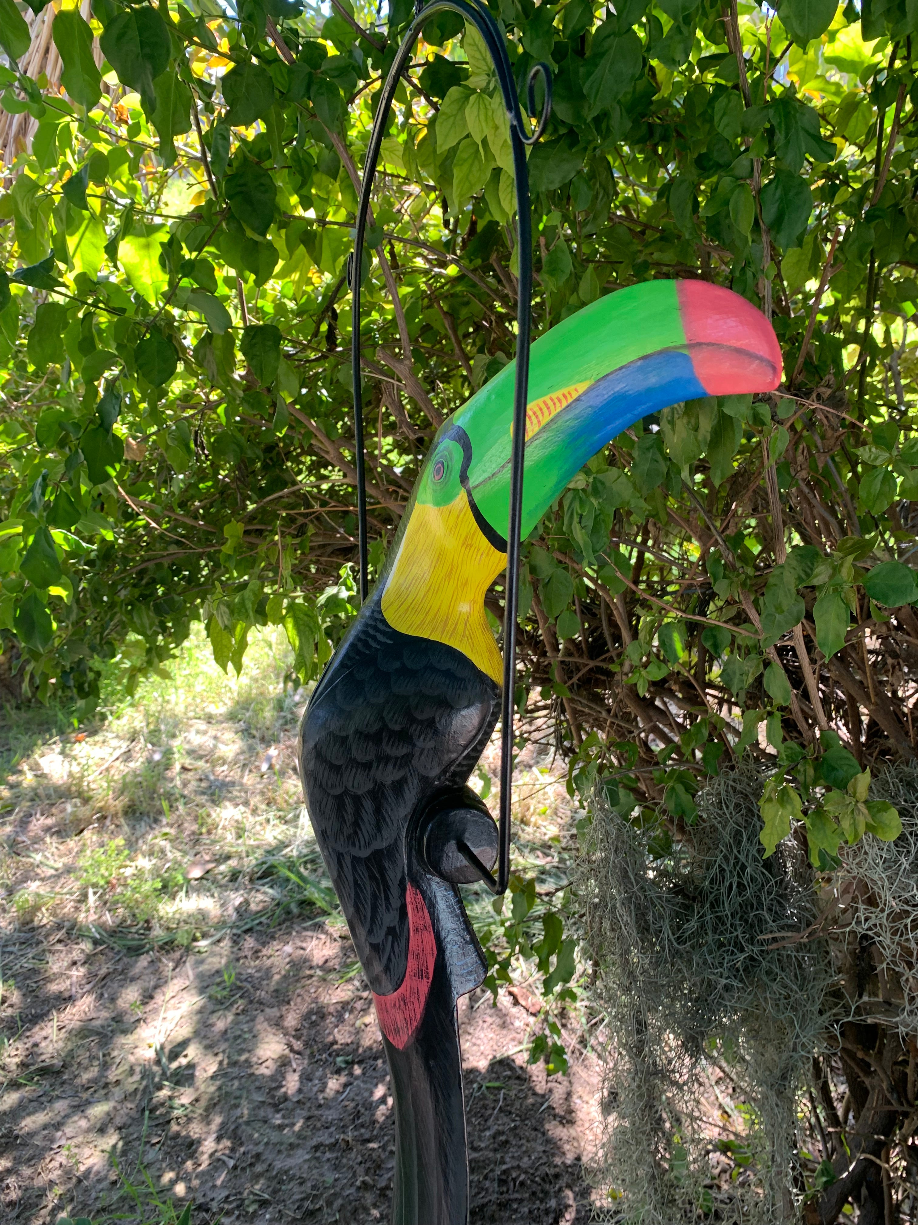 Colorful toucan garden ornament with rainbow beak hanging from a metal hook