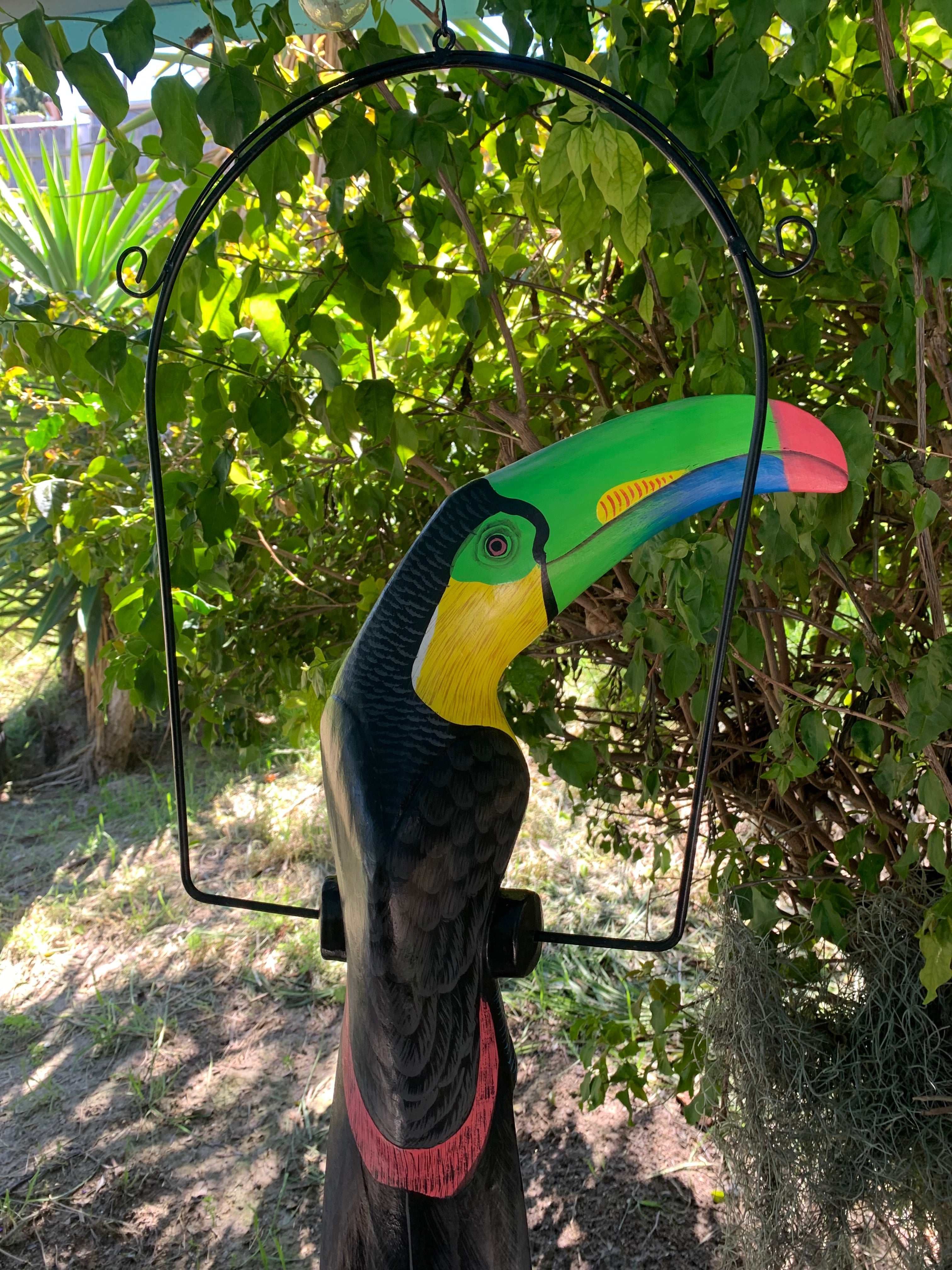 Colorful toucan garden sculpture with bright beak and black frame among green leaves.