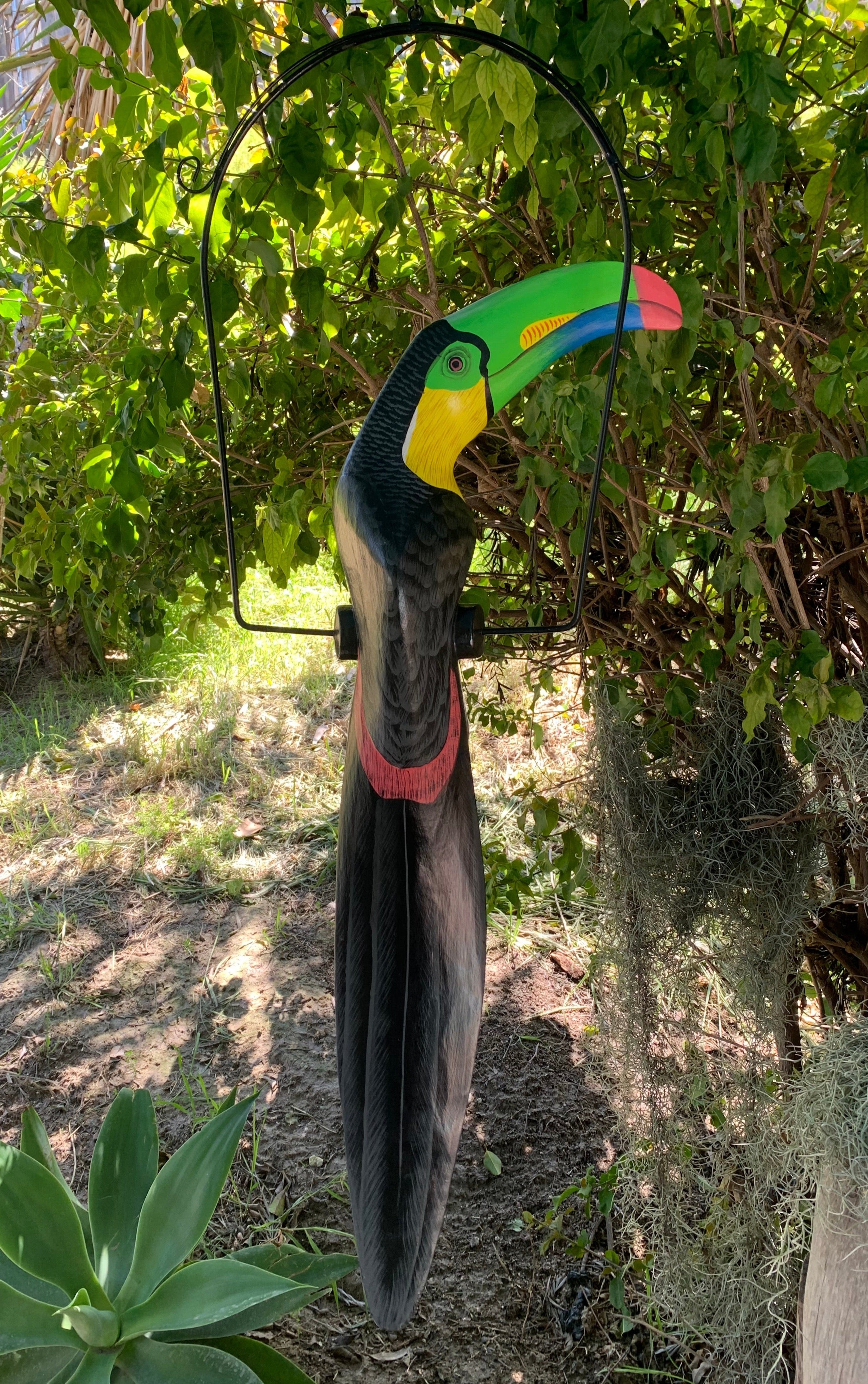 Colorful toucan garden statue with bright green beak under a circular metal hoop in a sunny yard
