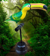 Bright green and yellow toucan sculpture perched on a stand in a lush jungle path.
