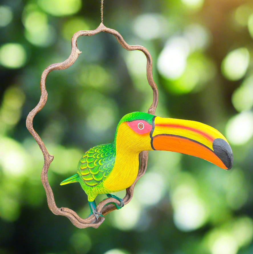 Vibrant toucan ornament with green body and orange beak hanging from a twisted branch.