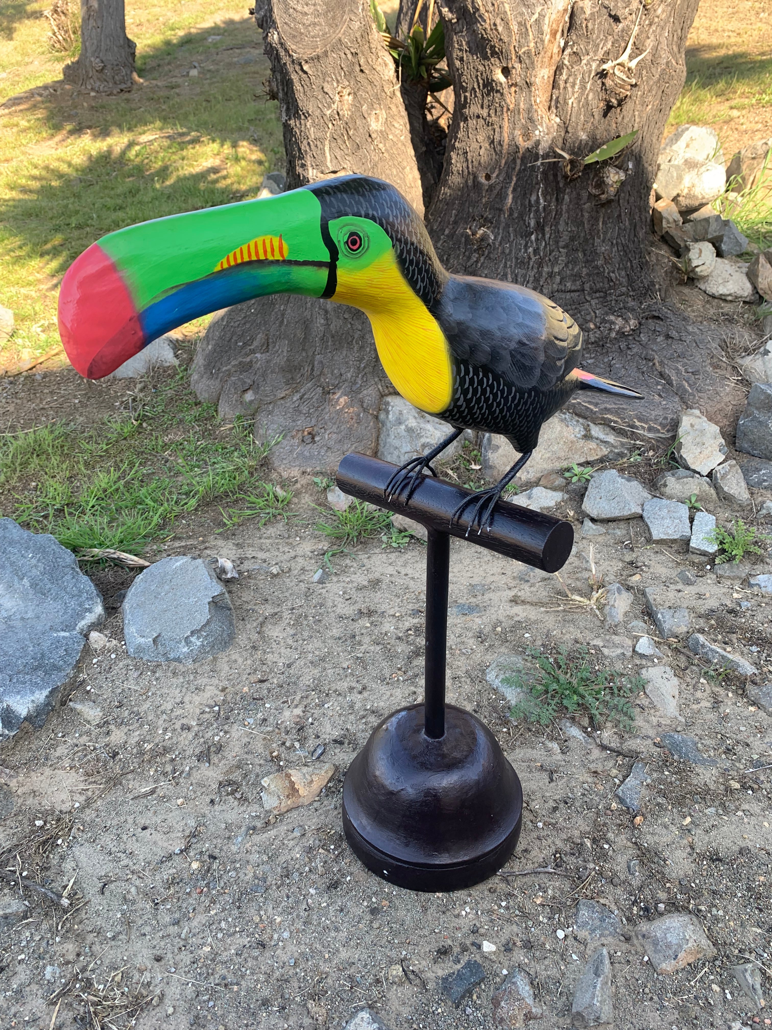 Colorful toucan sculpture with a large multicolor beak on a black stand outdoors