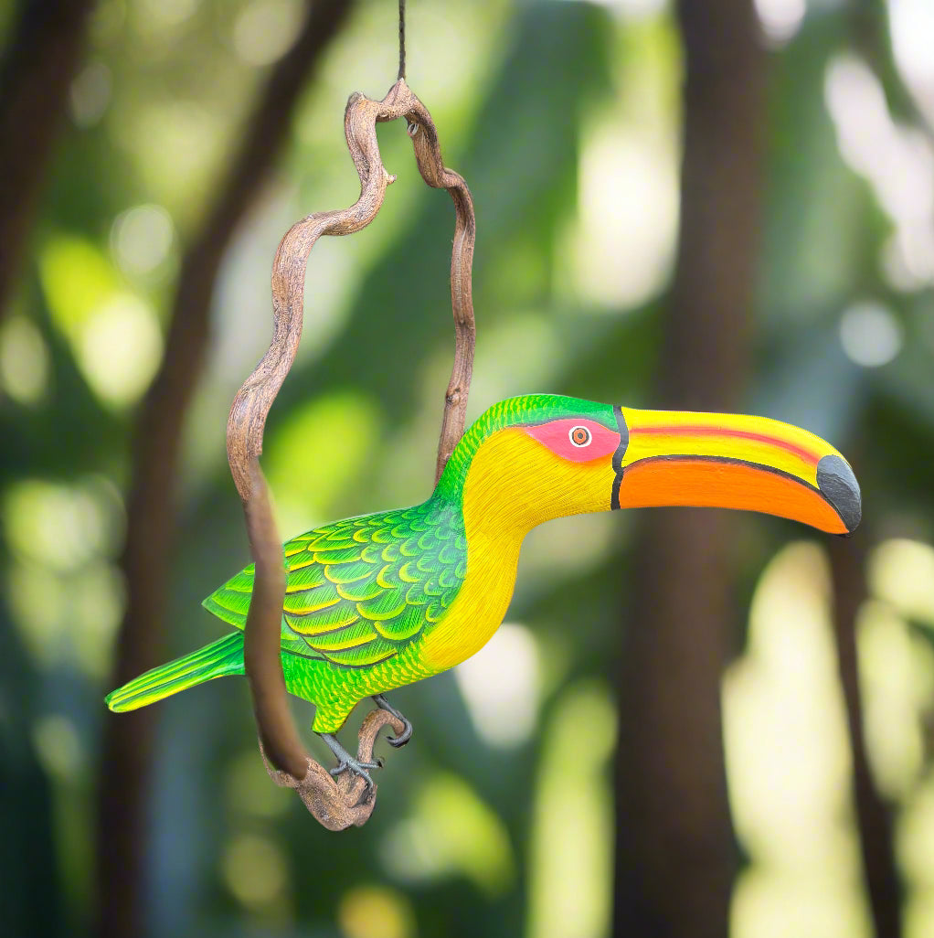 Colorful wooden toucan sculpture hanging from a vine in a garden