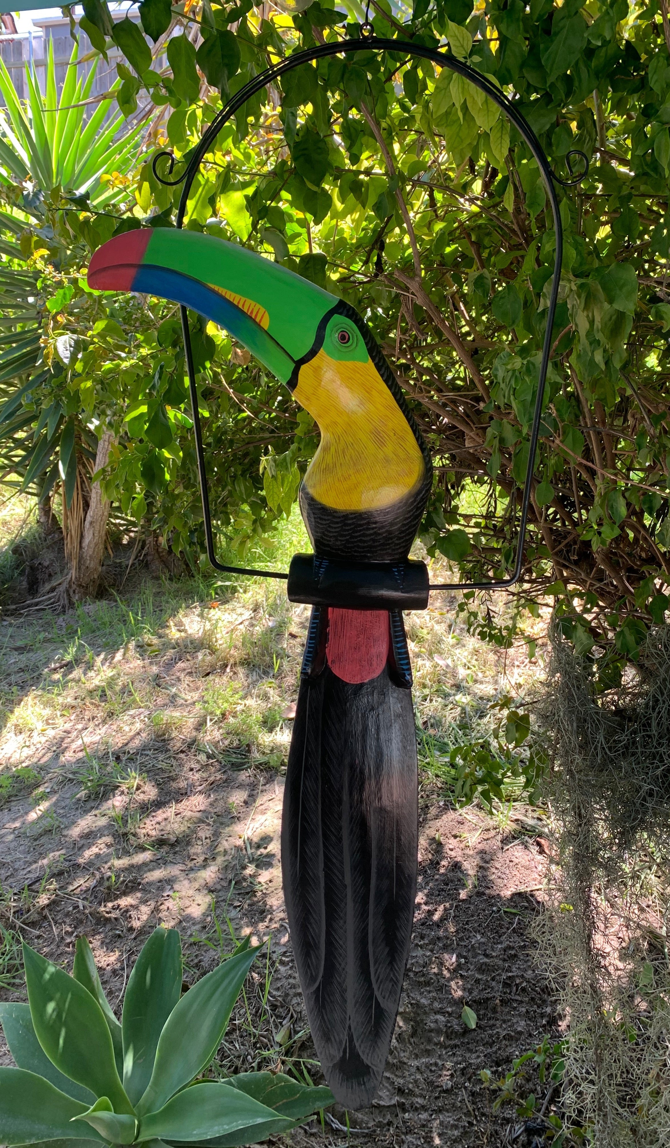 Colorful toucan sculpture hanging from a metal hoop in a garden
