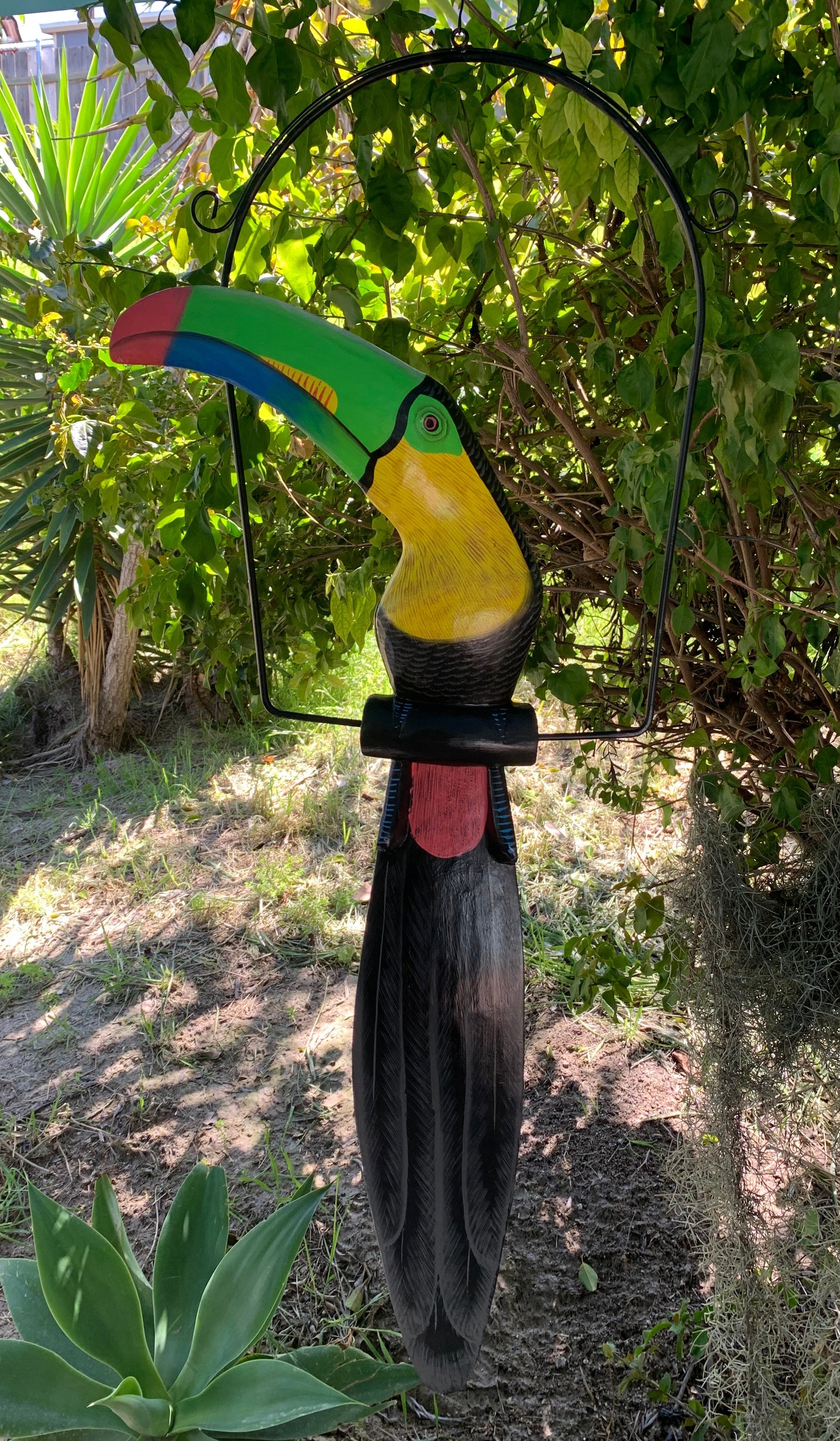 Colorful toucan sculpture hanging from a metal hoop in a garden