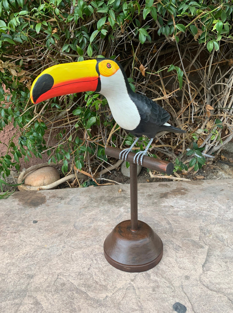 Colorful toucan sculpture perched on a wooden stand in front of a green hedge
