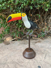 Colorful toucan sculpture perched on a wooden stand in front of a green hedge