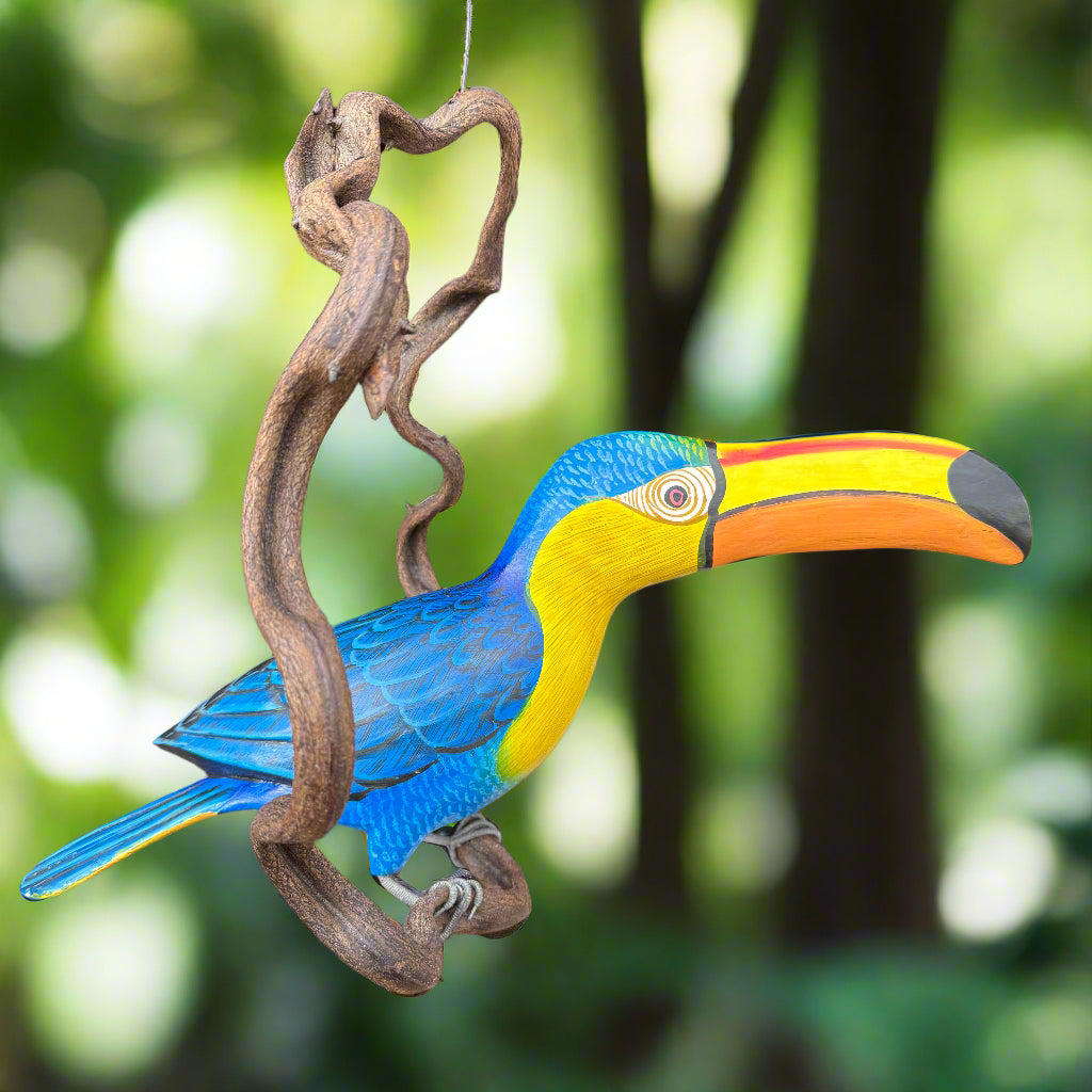 Colorful toucan sculpture perched on a twisted wooden branch with a green forest background