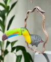 Colorful toucan sculpture perched on a twisted wooden branch.