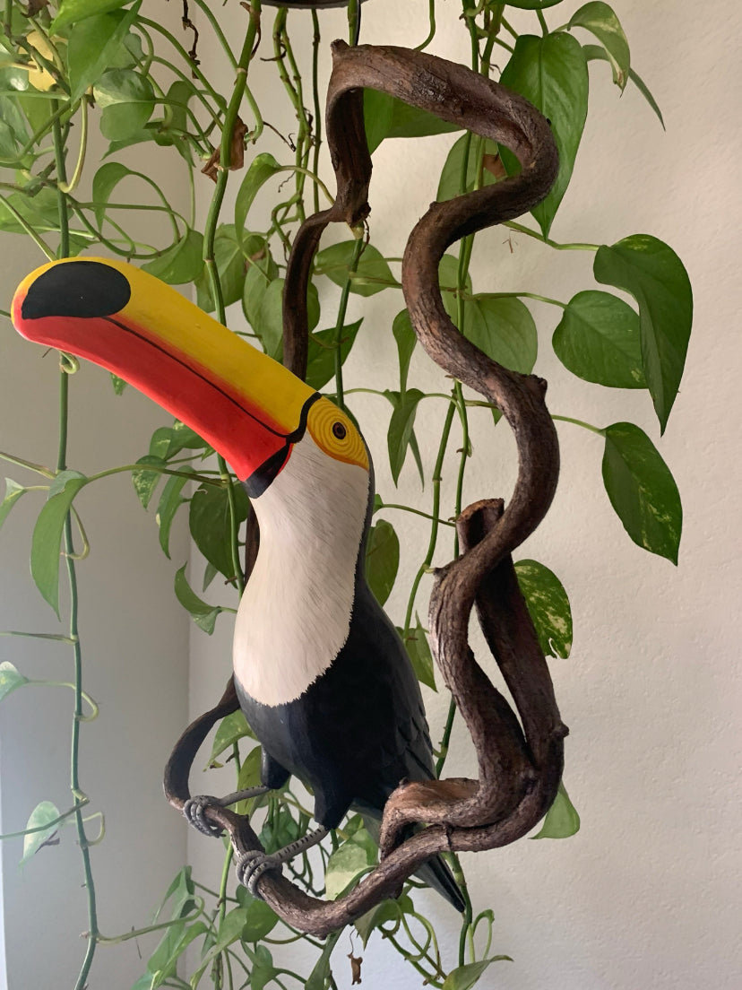 Colorful toucan statue perched on twisting indoor vine.