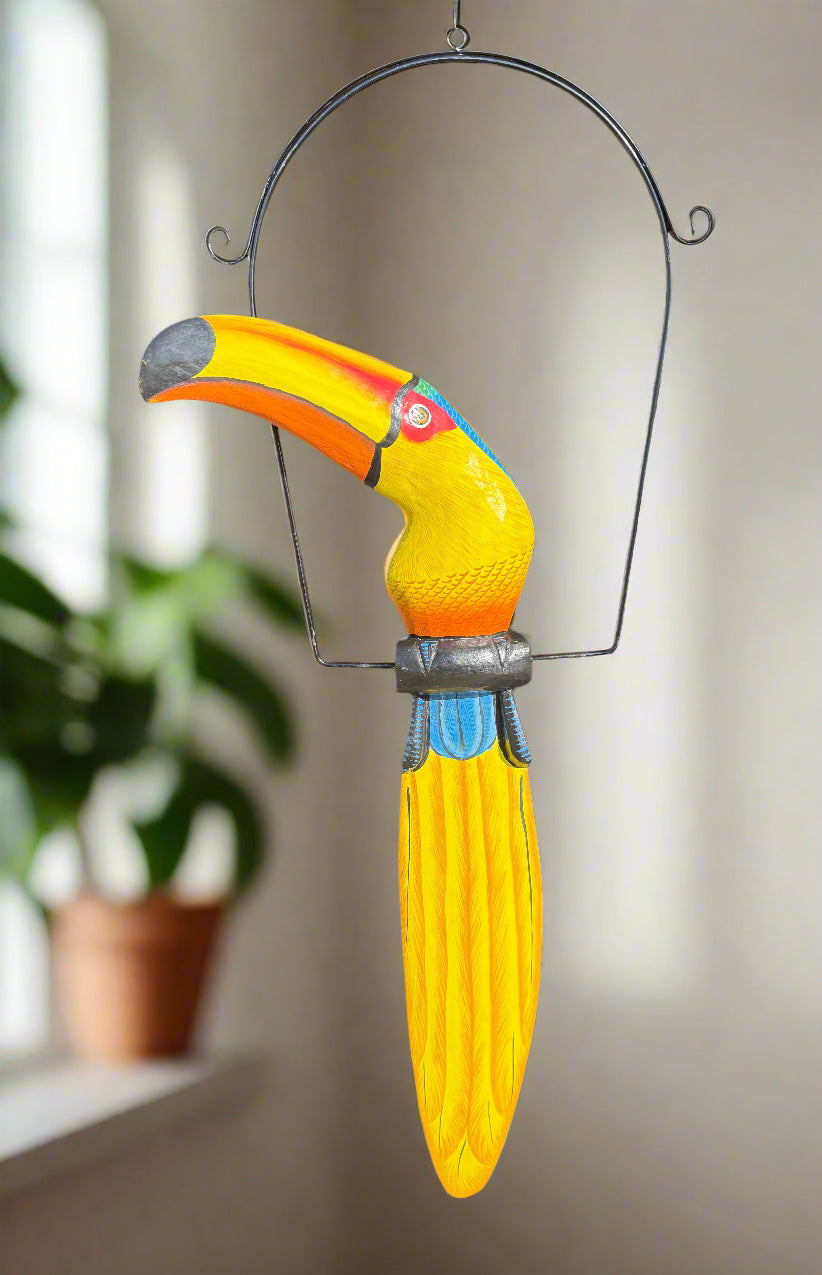 Colorful toucan wind chime with yellow body and orange beak hanging from a metal arch