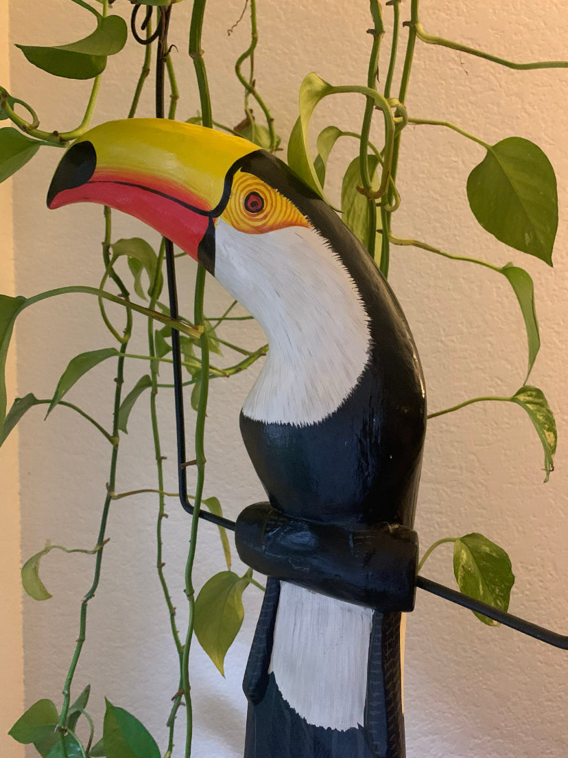 Colorful toucan sculpture with yellow beak and black-and-white body among green vines indoors