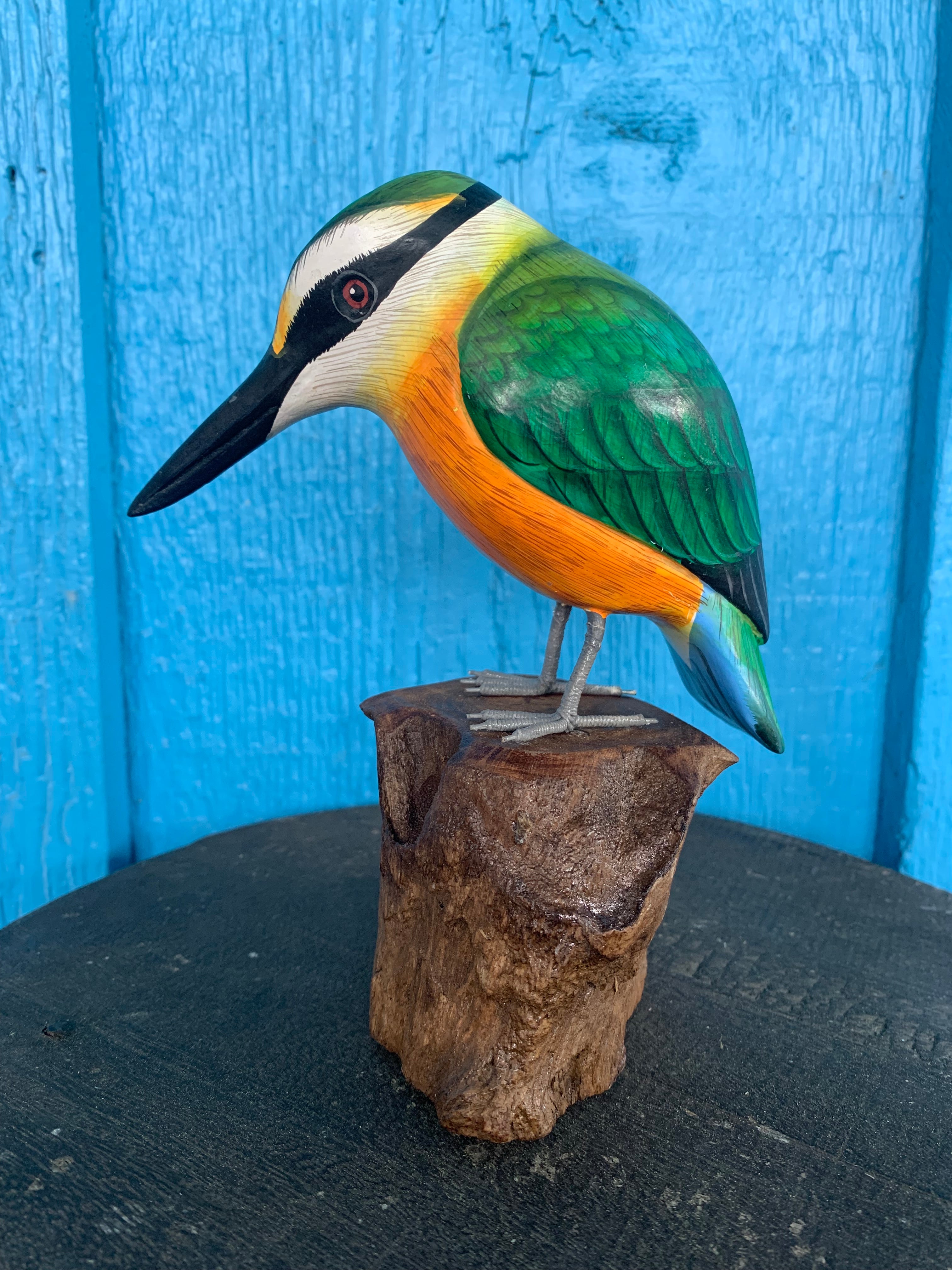 Colorful wooden kingfisher sculpture perched on a stump against a blue background