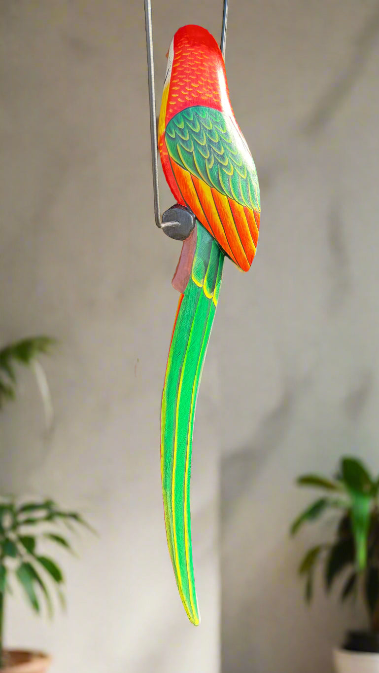 Vivid wooden parrot sculpture with red head, green wings, yellow accents, and a long striped tail.