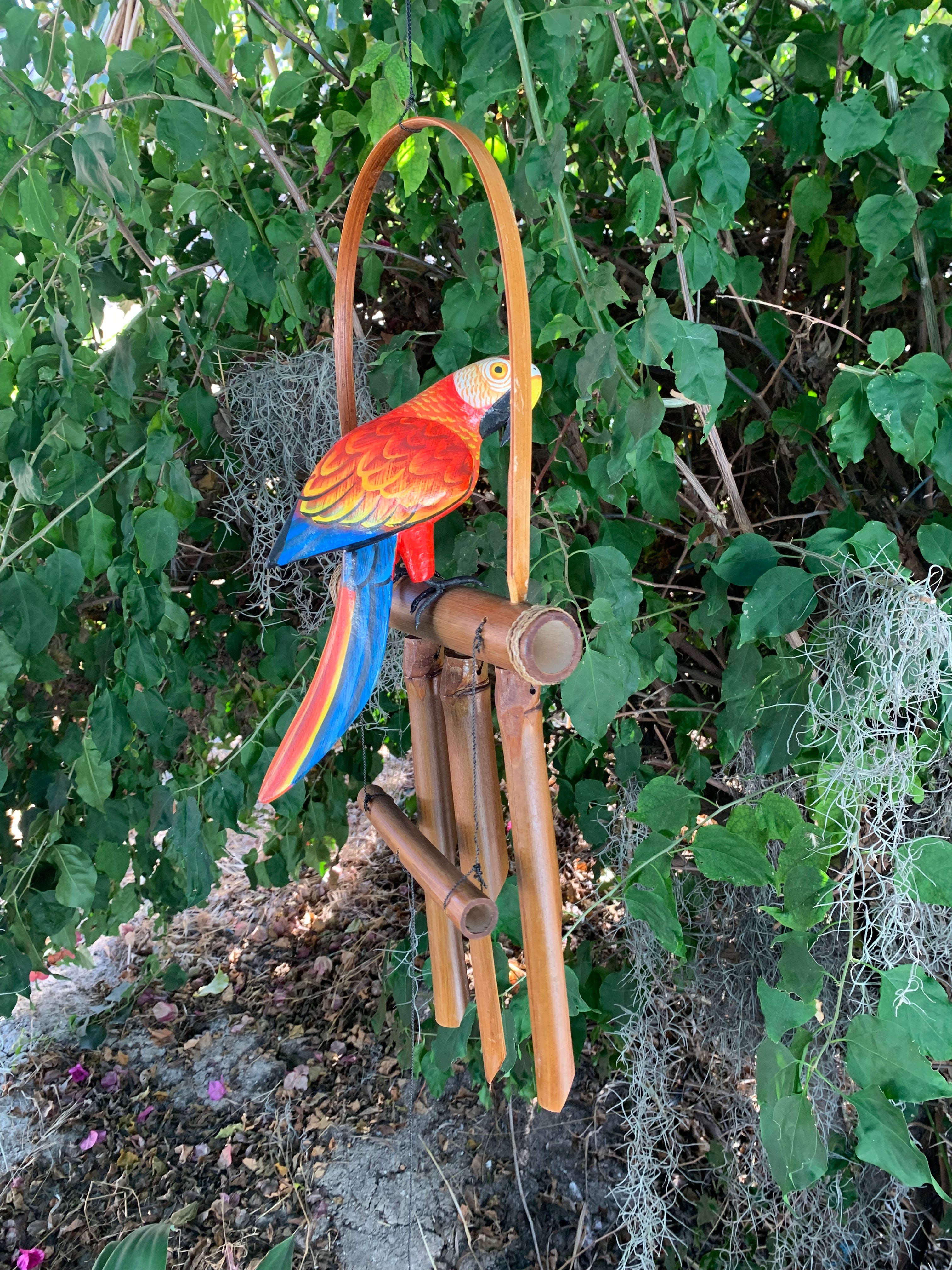 Colorful wooden parrot wind chime hanging on a bamboo frame among green garden vines