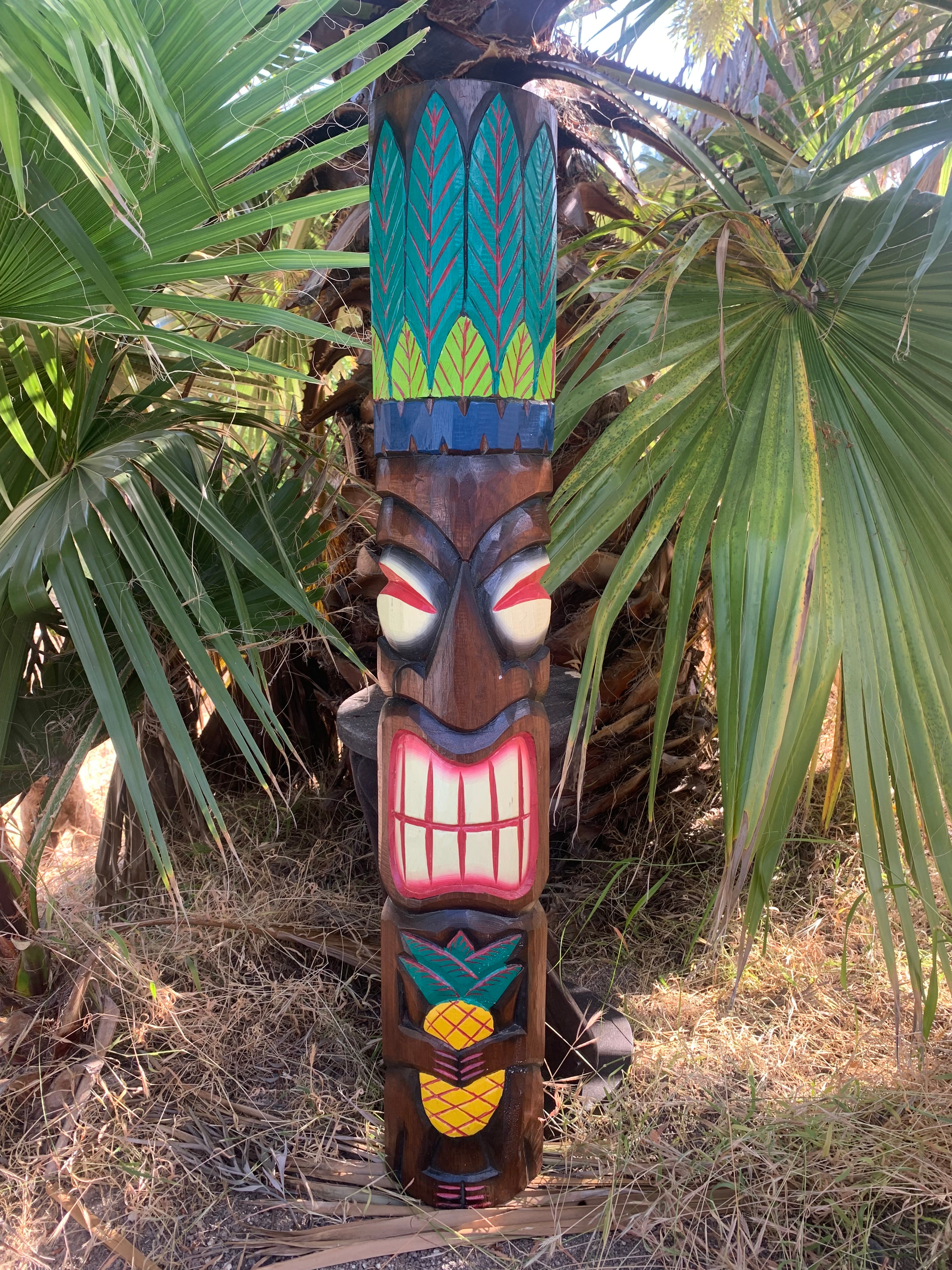 Colorful wooden tiki statue with oversized teeth among palm leaves