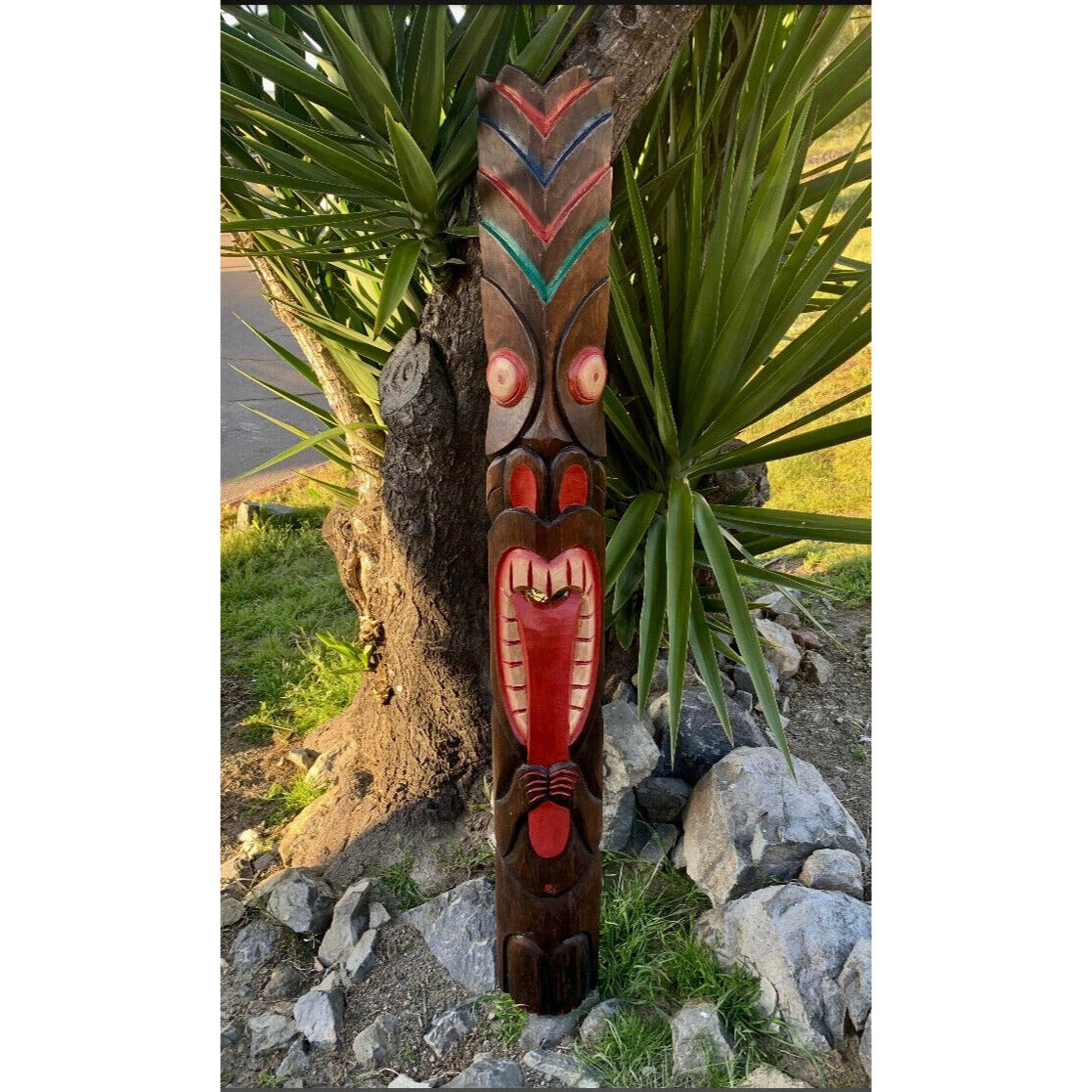 colorful wooden tiki totem pole with red and blue geometric patterns among rocks and tropical plants