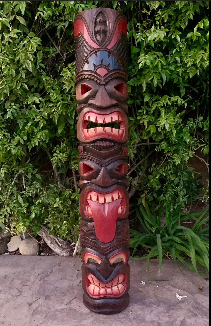 Colorful wooden totem pole carved with multiple faces in a garden
