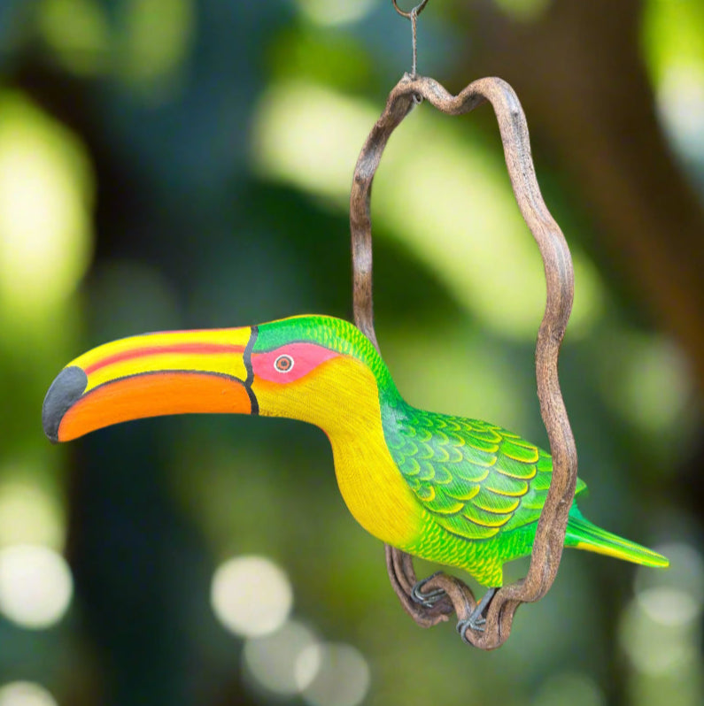 Colorful wooden toucan carving hanging from a vine with a bright orange beak and green body