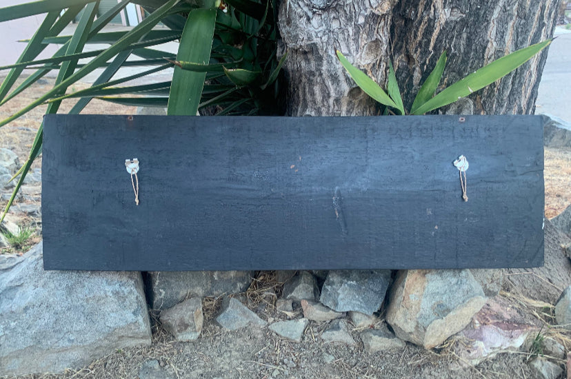dark slate sign leaning against rocks under a tree with two metal hooks