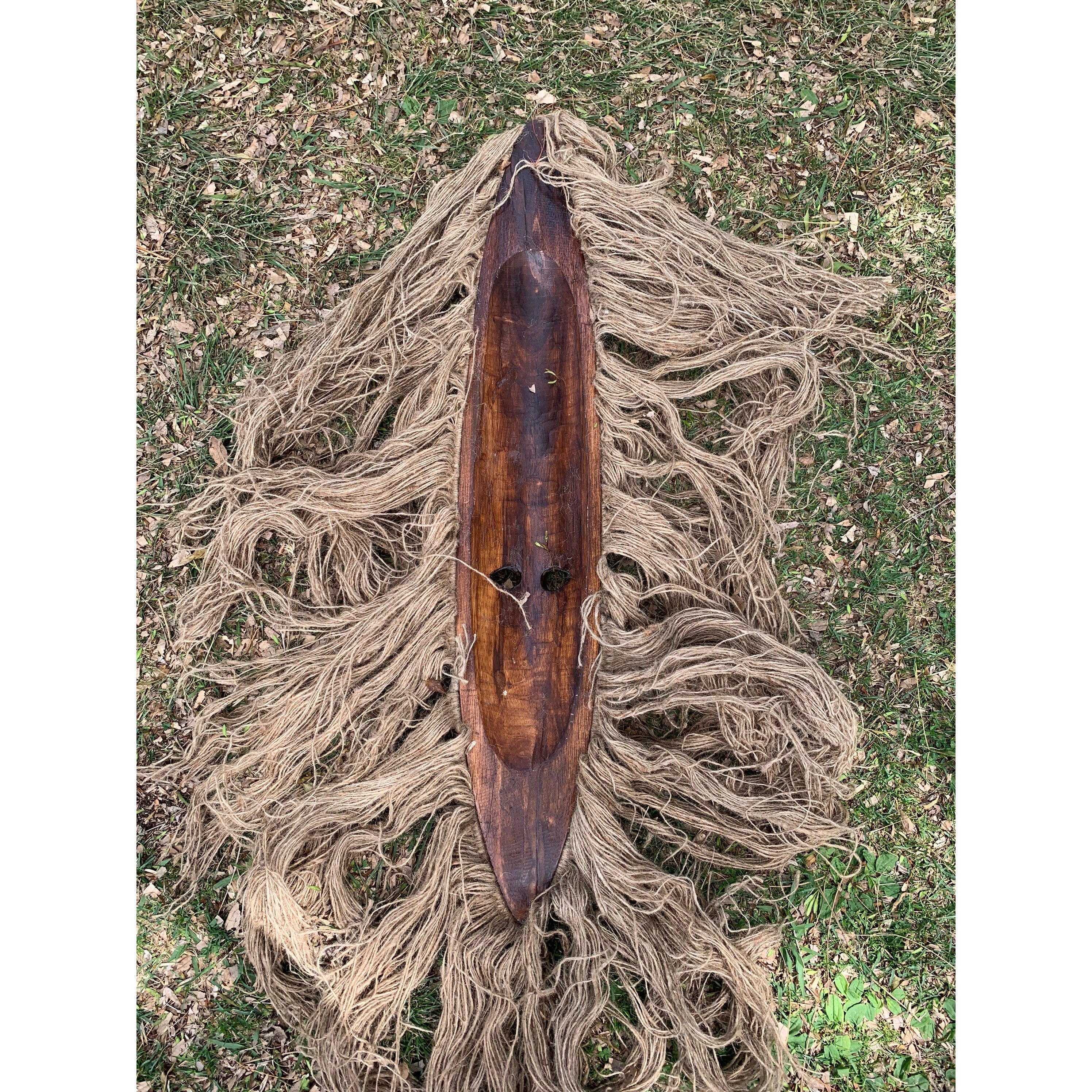 Dark wooden canoe resting on tangled beige rope on grass